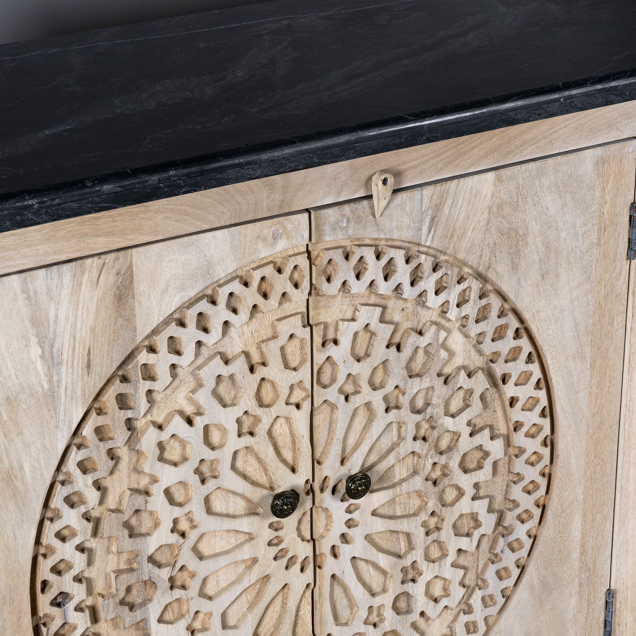 Close up image of a handcrafted acacia wood sideboard with black marble top and ornate hand-carved doors – a luxurious piece of wood carved furniture.