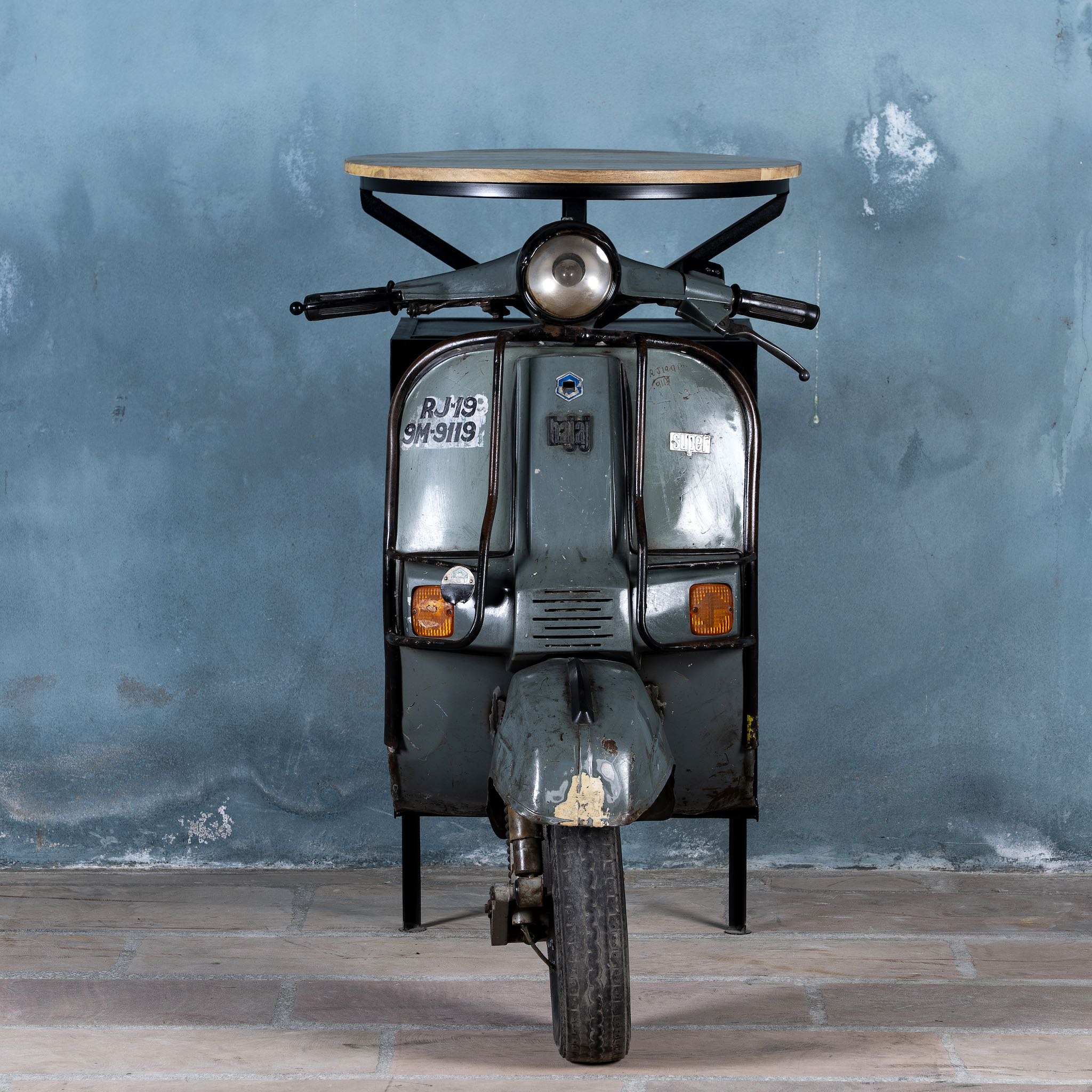 Front part image of a short bar table crafted from the front half of an original Bajaj scooter, featuring a round wooden top, metal frame, and rustic industrial finish.
