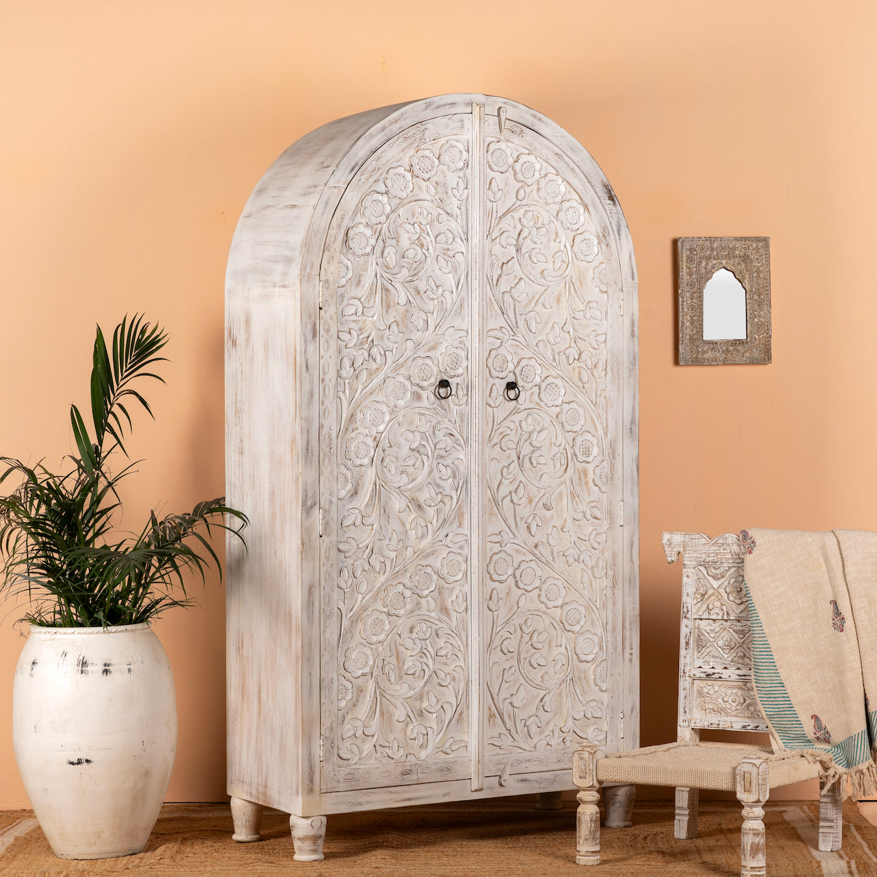 Side angle image of an arched wooden wardrobe made of mango wood with hand-carved floral details; hand carved wooden furniture in Ibiza style, 190 × 100 × 40 cm.
