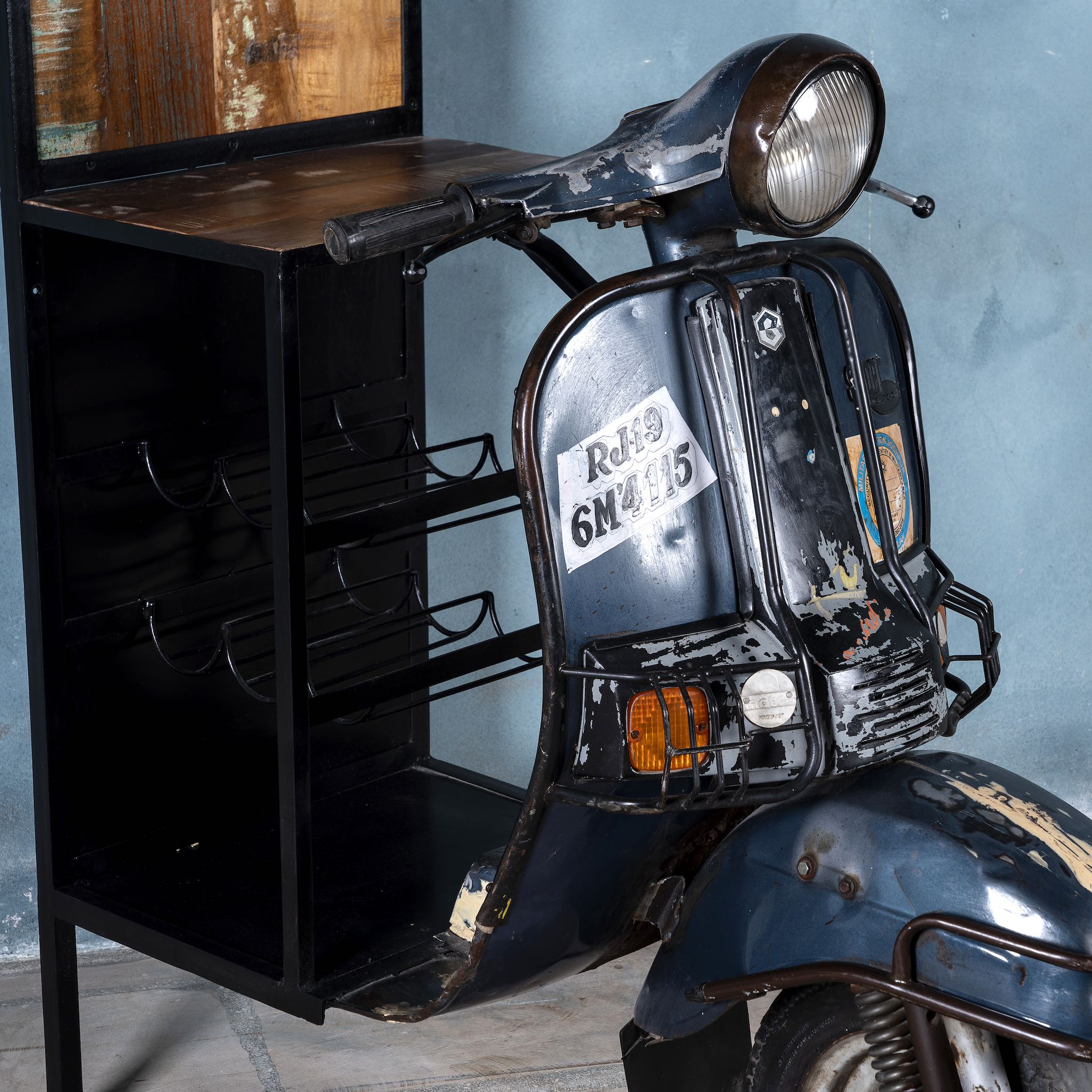 Close p image of a high bar table featuring the front half of a vintage Bajaj scooter, with tall wooden shelving and an industrial metal frame, designed for stylish bar storage.