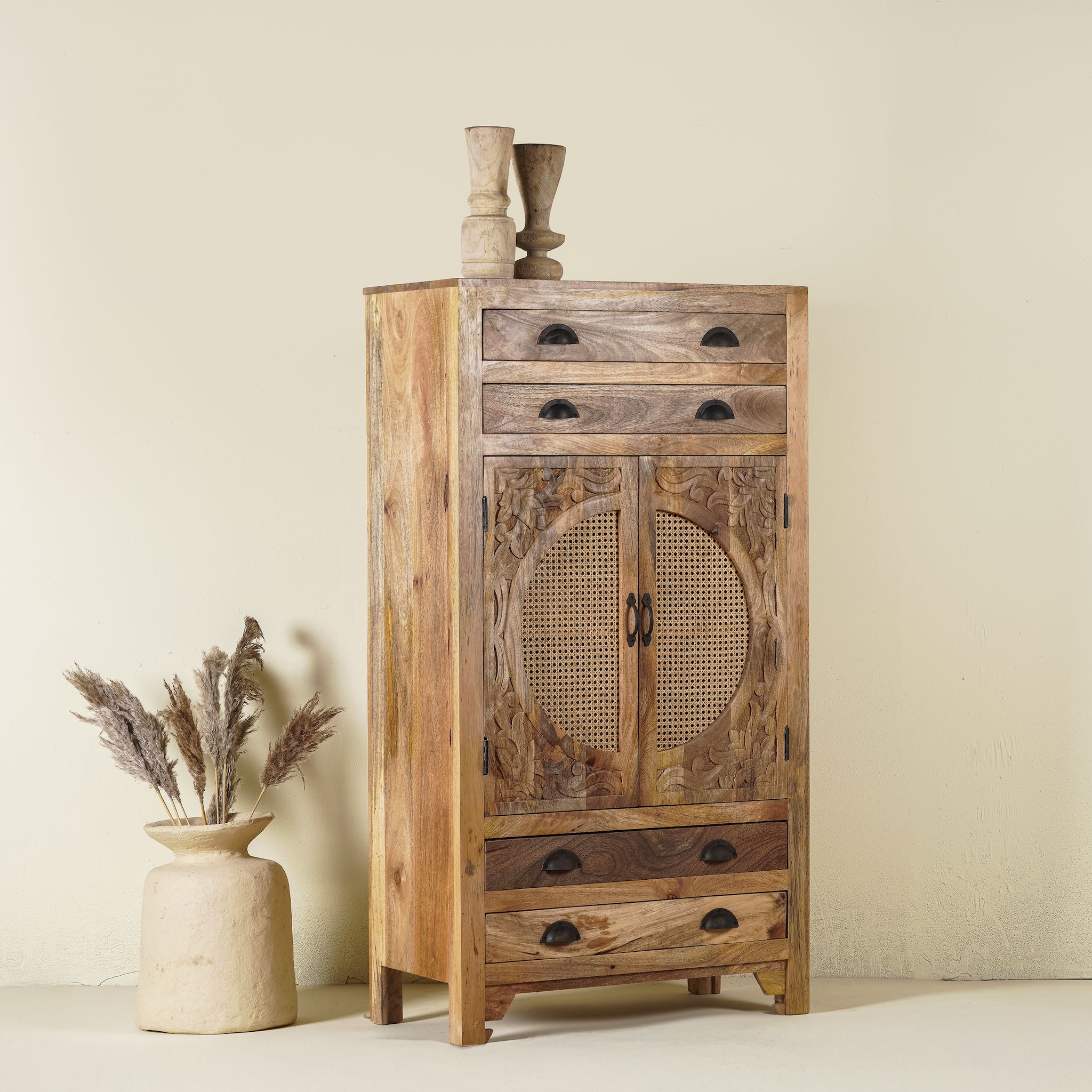 Side angle image of a handcrafted mango wood cabinet Agnayi with rattan inserts and floral carvings, rattan furniture for bohemian interior, 80 × 40 × 148 cm.