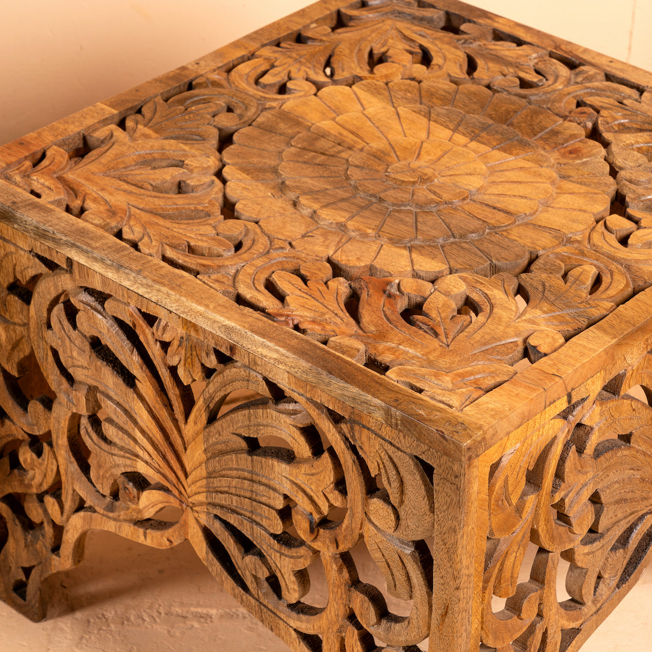 Close up image of a square hand carved coffee table made from solid mango wood with intricate detailing; compact and rustic, 50 × 50 × 40 cm.