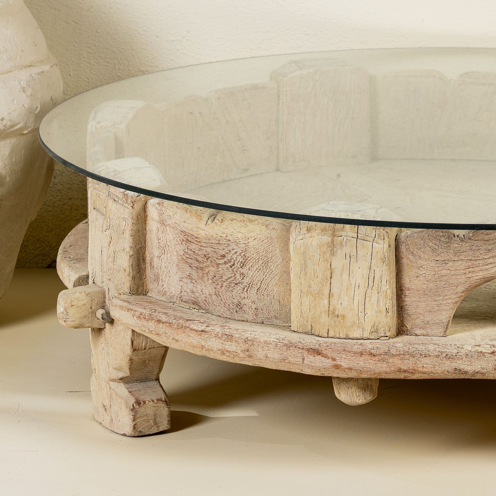 Close up image of a round reclaimed teak coffee table with glass top and hand-carved base; rustic vintage design, 84 cm diameter, 28 cm height.