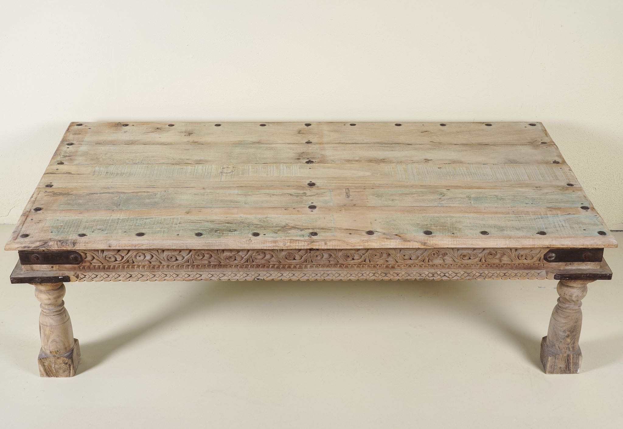 Close up image of the table top of the rustic coffee table Amana made from old reclaimed teak wood, featuring a weathered finish, turned legs, decorative carved apron, and visible metal rivets, styled with earthy decor in a minimal interior setting.