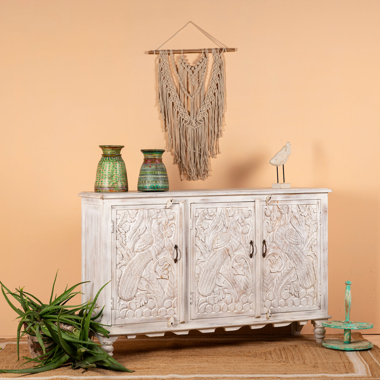 Side angle image of a hand-carved mango wood sideboard with peacock and foliage motifs, whitewashed finish; perfect for Indian home decor, 150 × 95 × 40 cm.