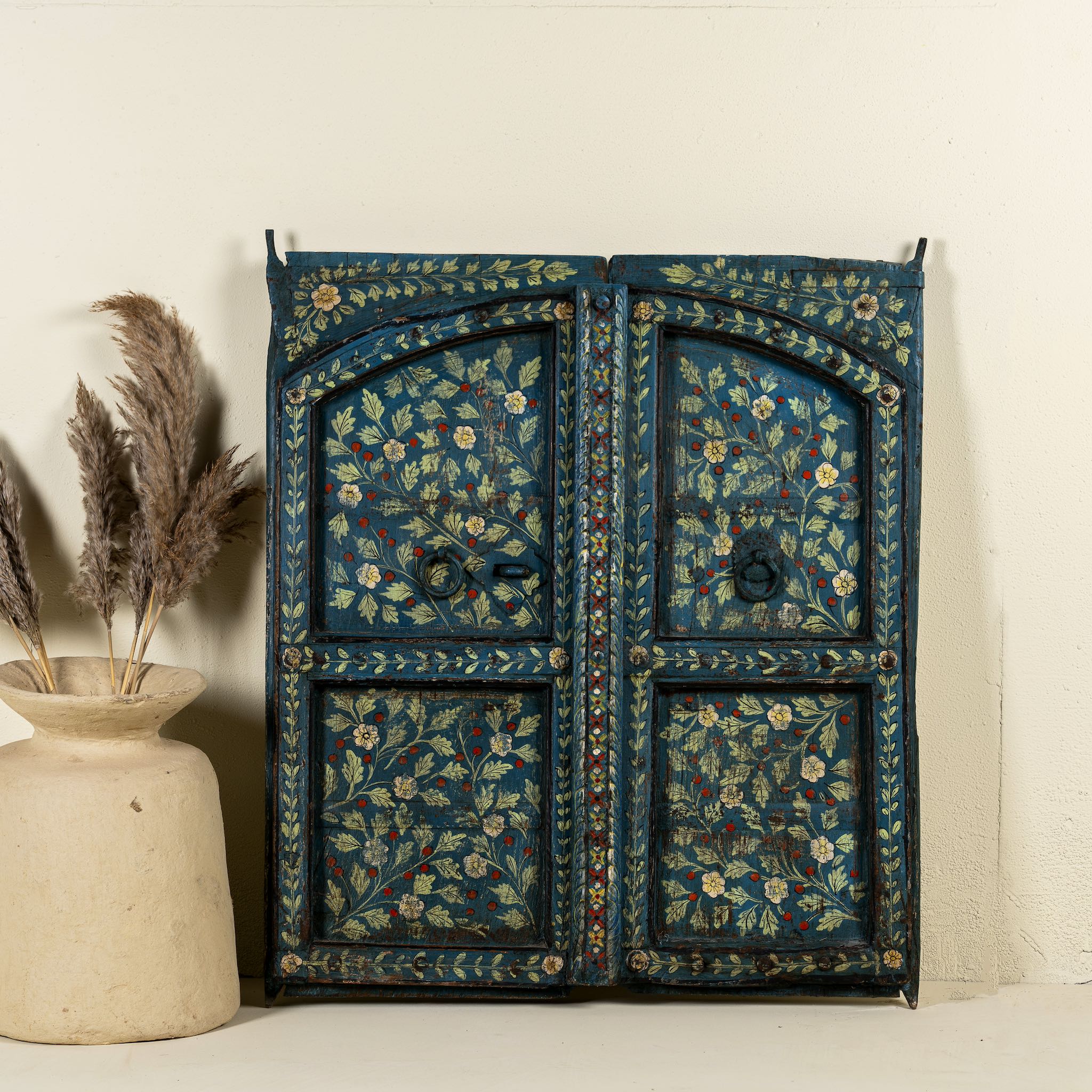 Vintage wall panel crafted from an old teak wood window frame, hand-painted with detailed floral designs in cream, red, and green on a rich teal background, featuring arched upper panels and decorative metal ring pulls.