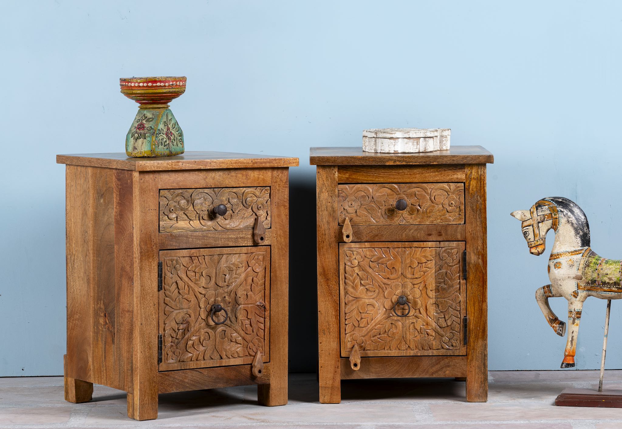 Side angle image of a hand-carved mango wood bedside tables with floral motifs – a set of carved wooden furniture perfect for rustic and relaxed interiors.