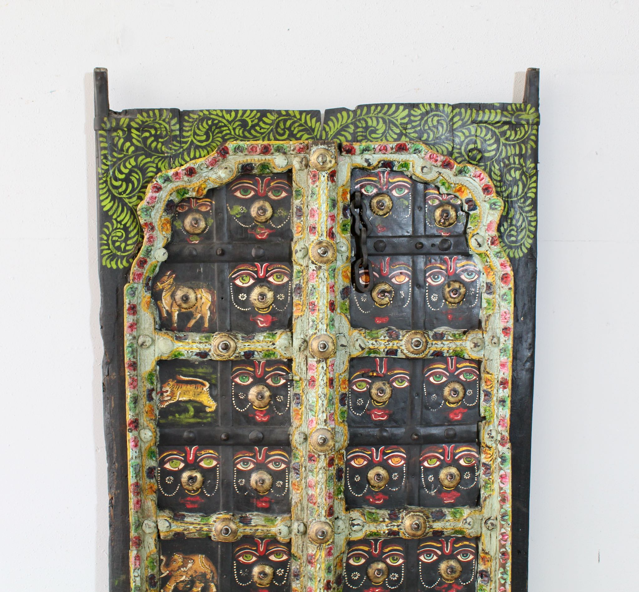 Close up image of a hand-painted Indian antique teak door panel with sacred animal motifs and face masks, vintage wall panels repurposed as home decor.