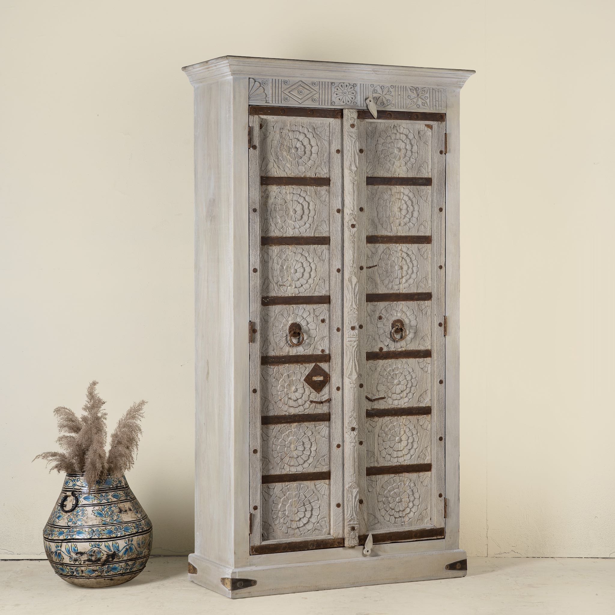 Side angle image of a old door cabinet with reclaimed teak doors, floral carvings, and iron accents; artisan teak wood wardrobe with mango wood frame, 100 × 44 × 206 cm.