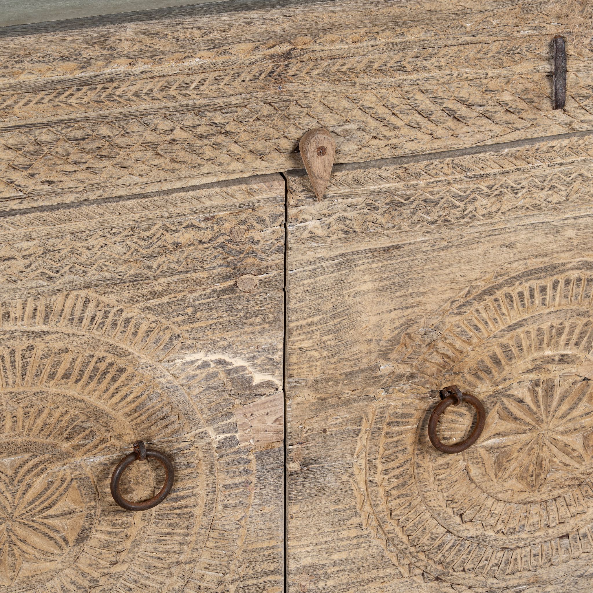 Close up picture of a sideboard with hand-carved teak wood front, sandblasted for a sun-worn finish — a unique piece in rustic Ibiza style with circular mandala carvings and iron ring handles.
