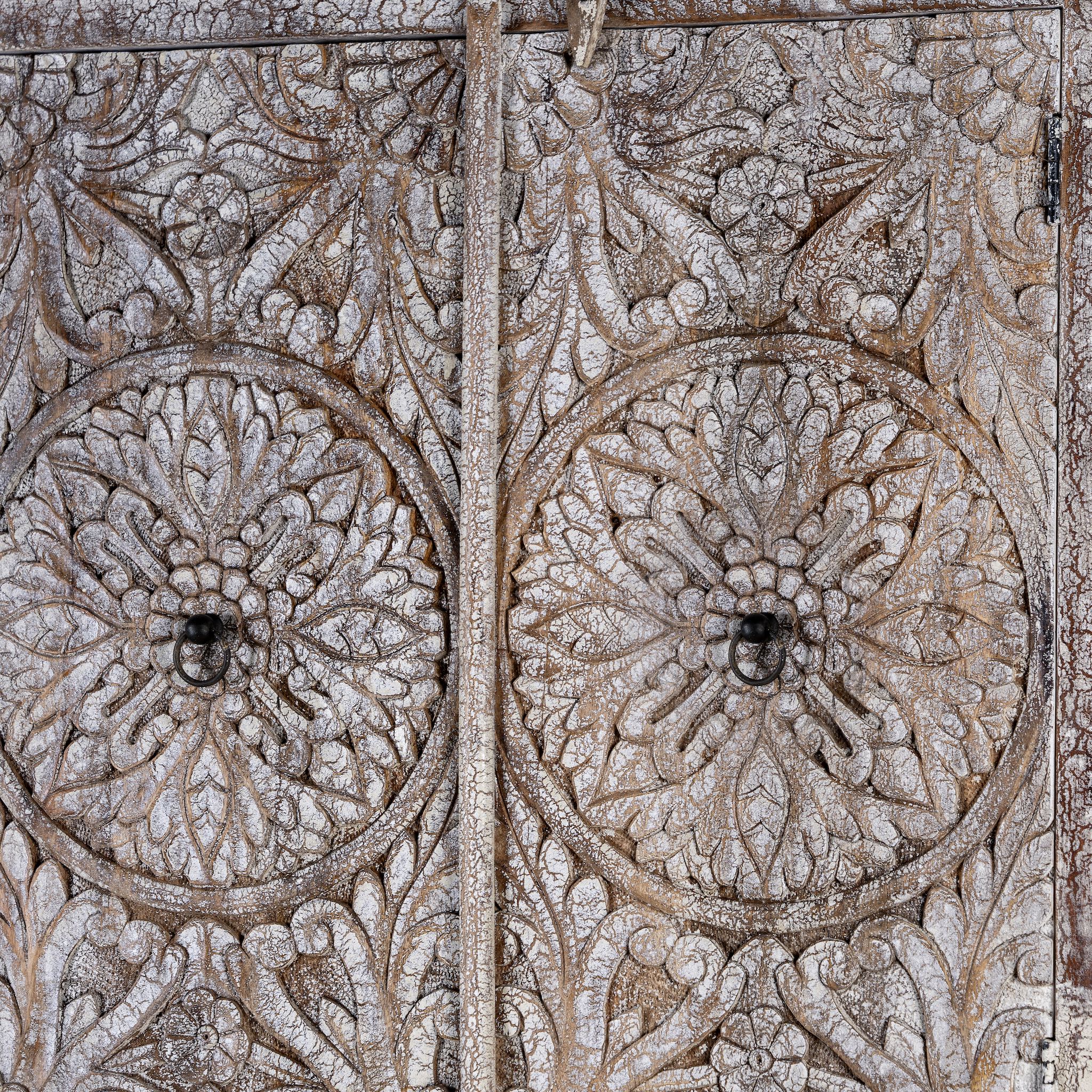 Close up picture of a hand-carved acacia wood wardrobe with floral detailing and distressed finish – vintage living room furniture with artisan craftsmanship.