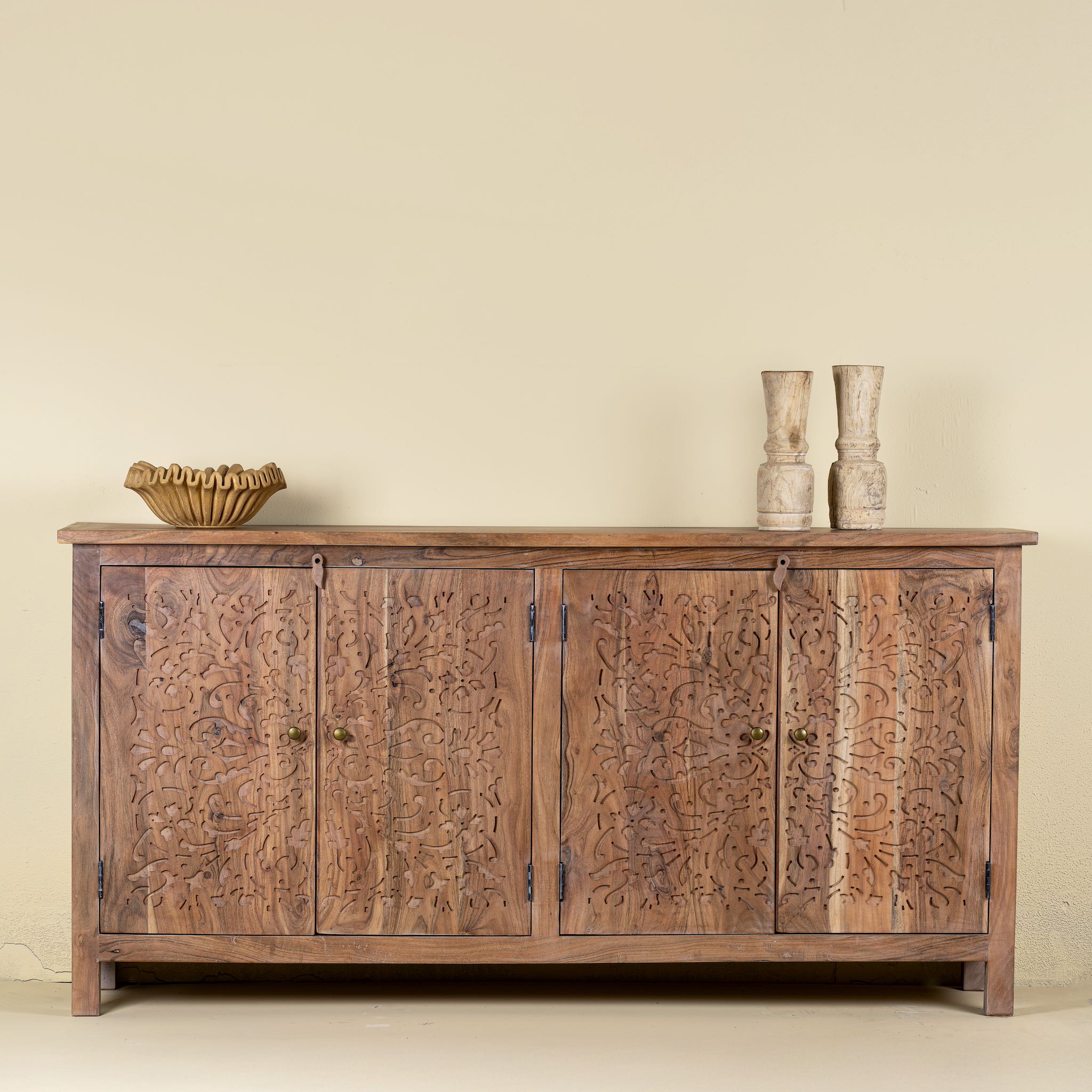 Font view of an acacia wood sideboard with floral carvings over all 4 doors and brass fitted door handles.