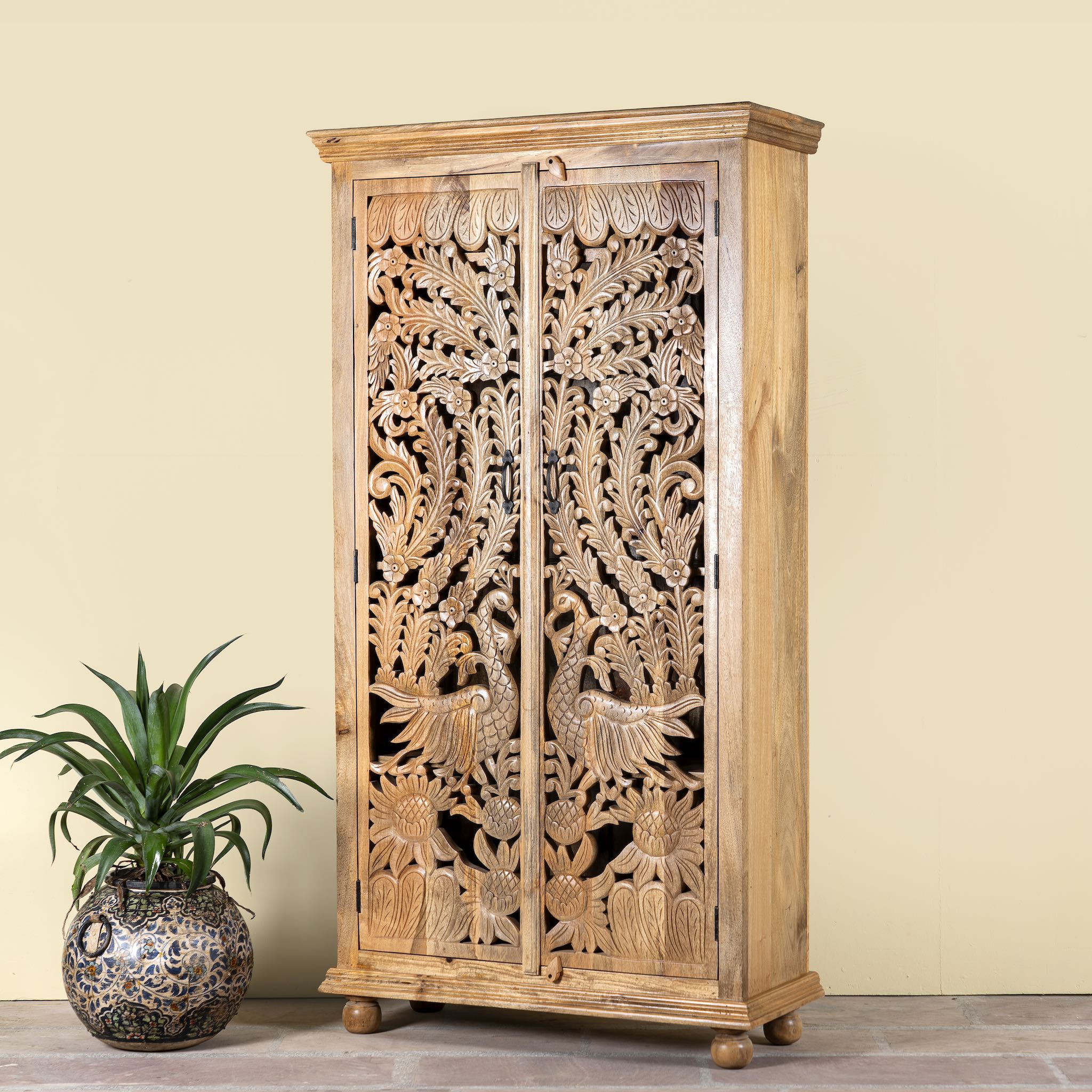 Side angle image of a hand-carved mango wood cupboard with Indian peacock design motifs, Mediterranean-style wardrobe; elegant mango wood furniture, 190 × 100 × 40 cm.