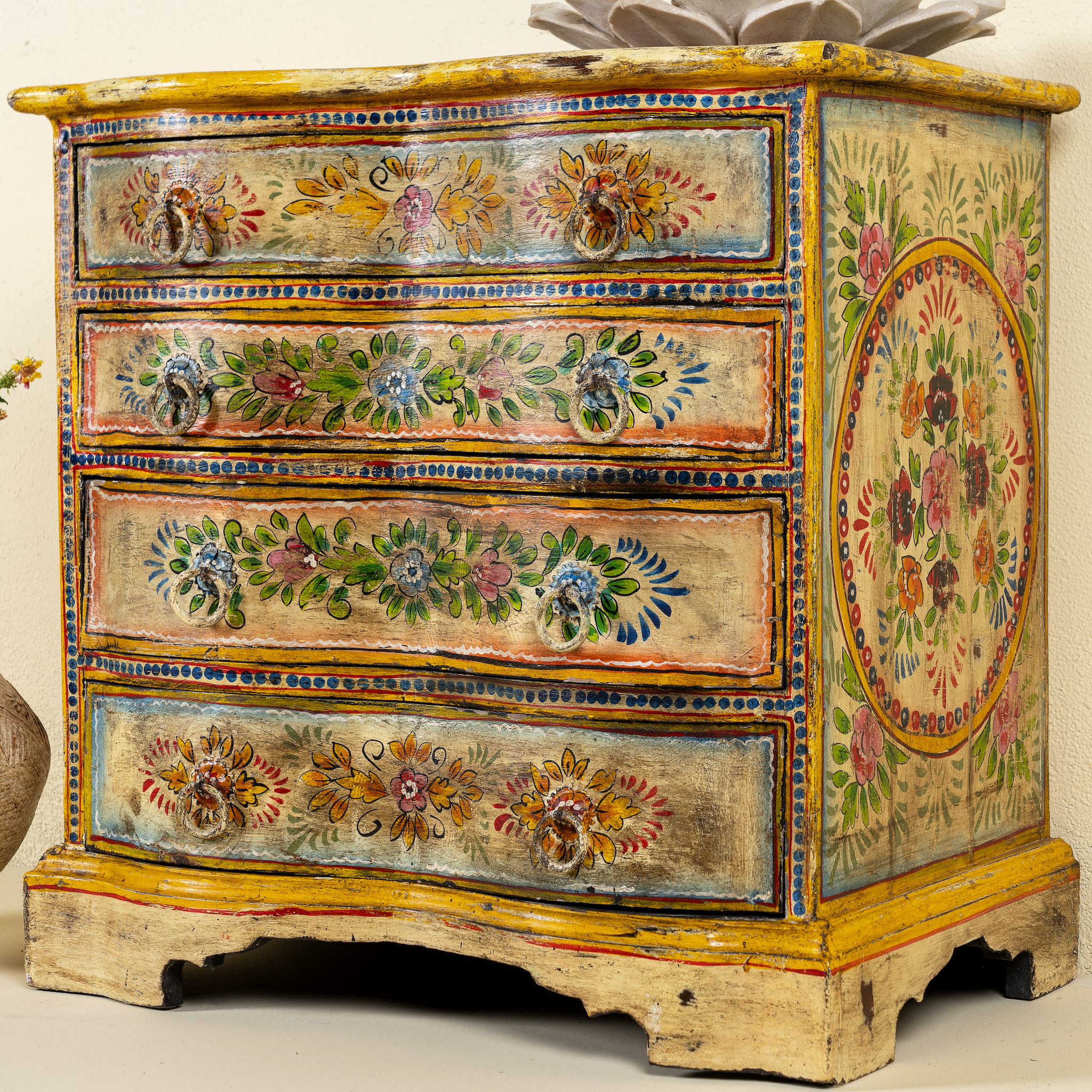 Close up side angle image of a hand-painted reclaimed wood chest of drawers with floral designs and distressed antique finish; perfect for bohemian interiors and vintage hand painted furniture lovers.