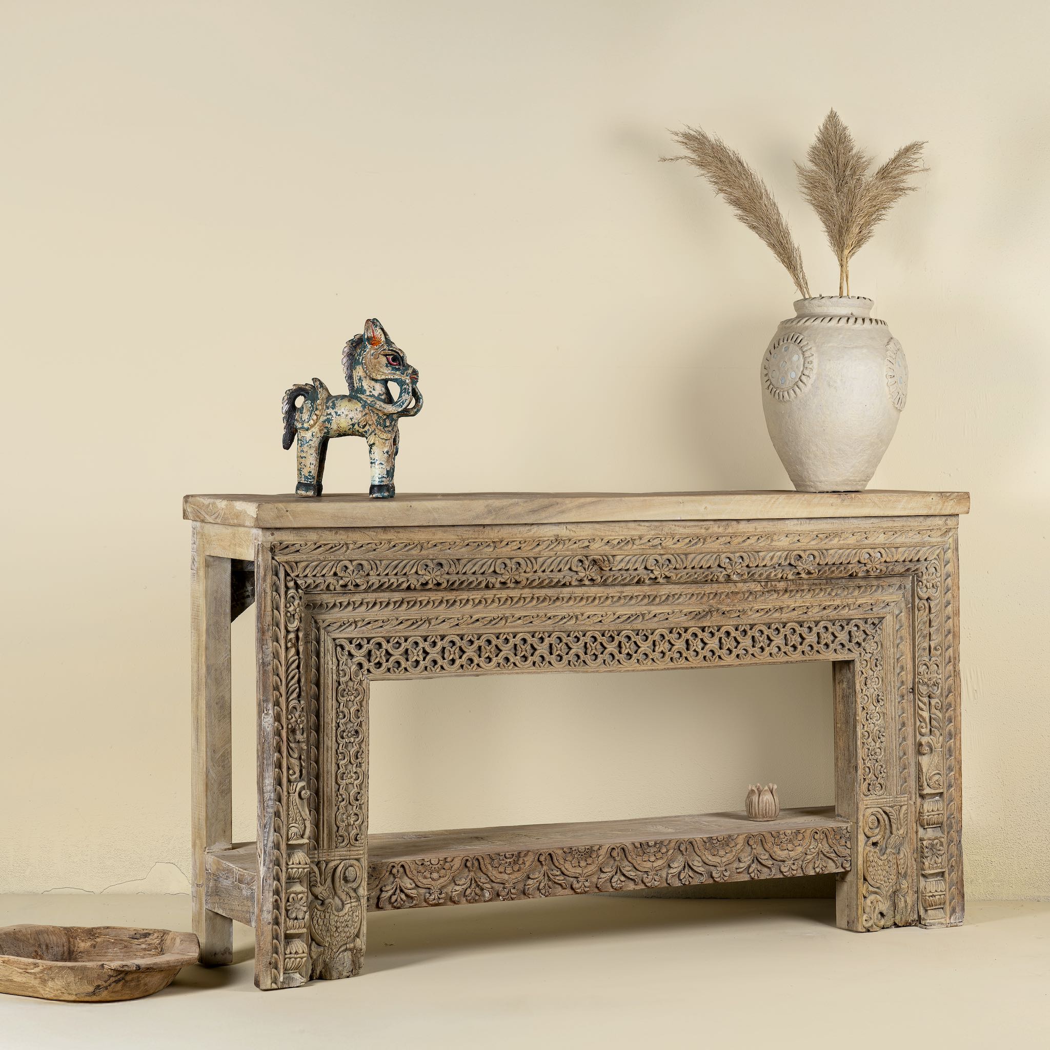 Side angle image of a ornate console table crafted from reclaimed teak wood and refurbished architectural elements, featuring intricate hand-carved detailing with floral and geometric motifs, showcasing a vintage artisanal aesthetic.