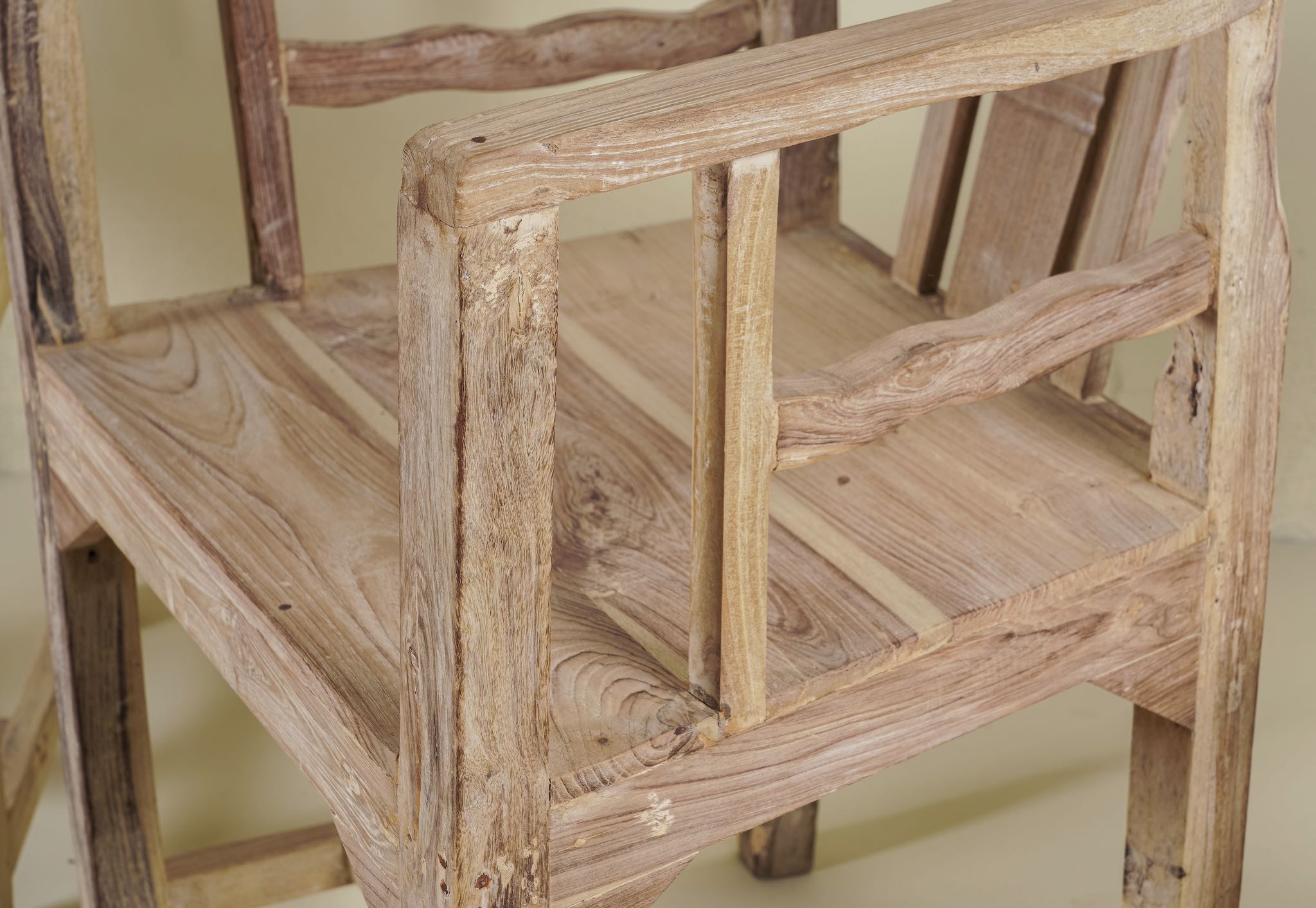 Close up image of a rustic-style armchair made from reclaimed teak wood, featuring a natural, unfinished look with visible wood grain and variations in tone, and a curved backrest with vertical slats.