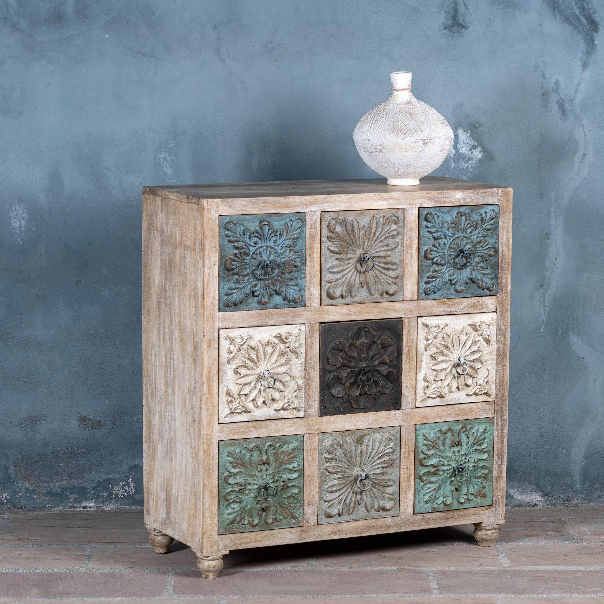 Side angle view of a Chest of 9 drawers made from mango wood, featuring hand-carved floral fronts in a mix of turquoise, black, and natural tones, a vibrant statement piece with vintage charm.