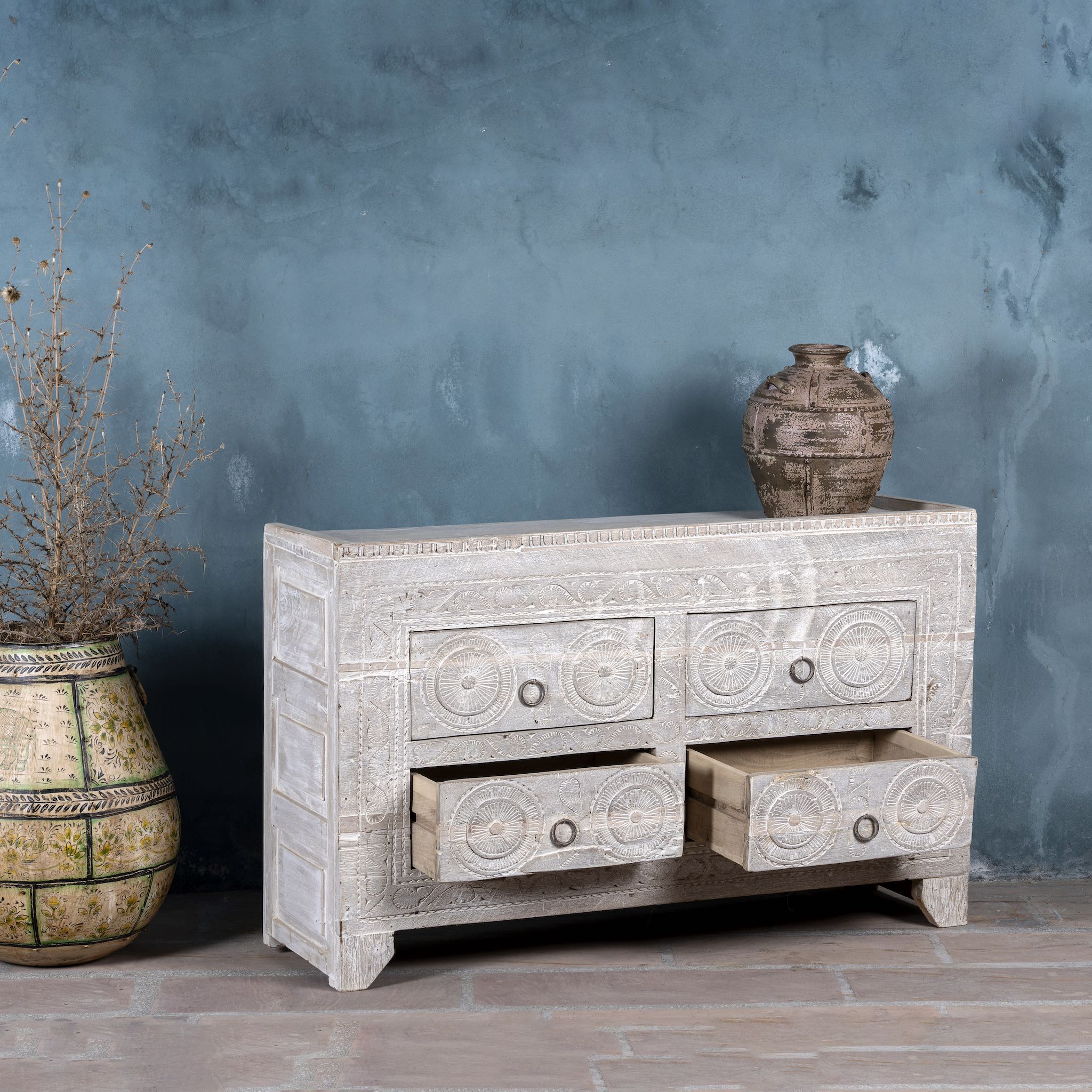 Wooden dresser with carved designs against a textured blue wall.