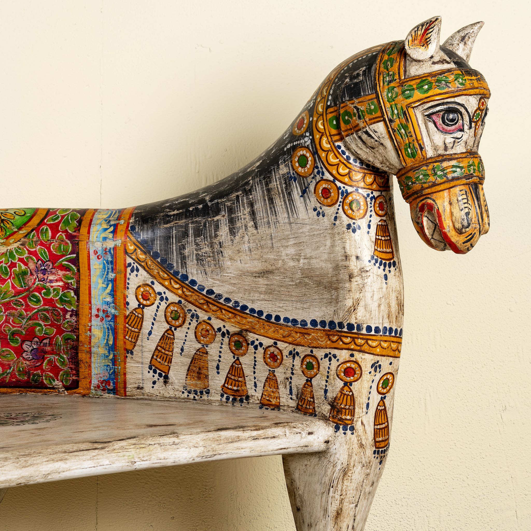 Close up image of the head of a hand-painted reclaimed wood chair-style horse bench with double carvings; unique furniture for a bohemian interior, 160 × 70 × 90 cm.