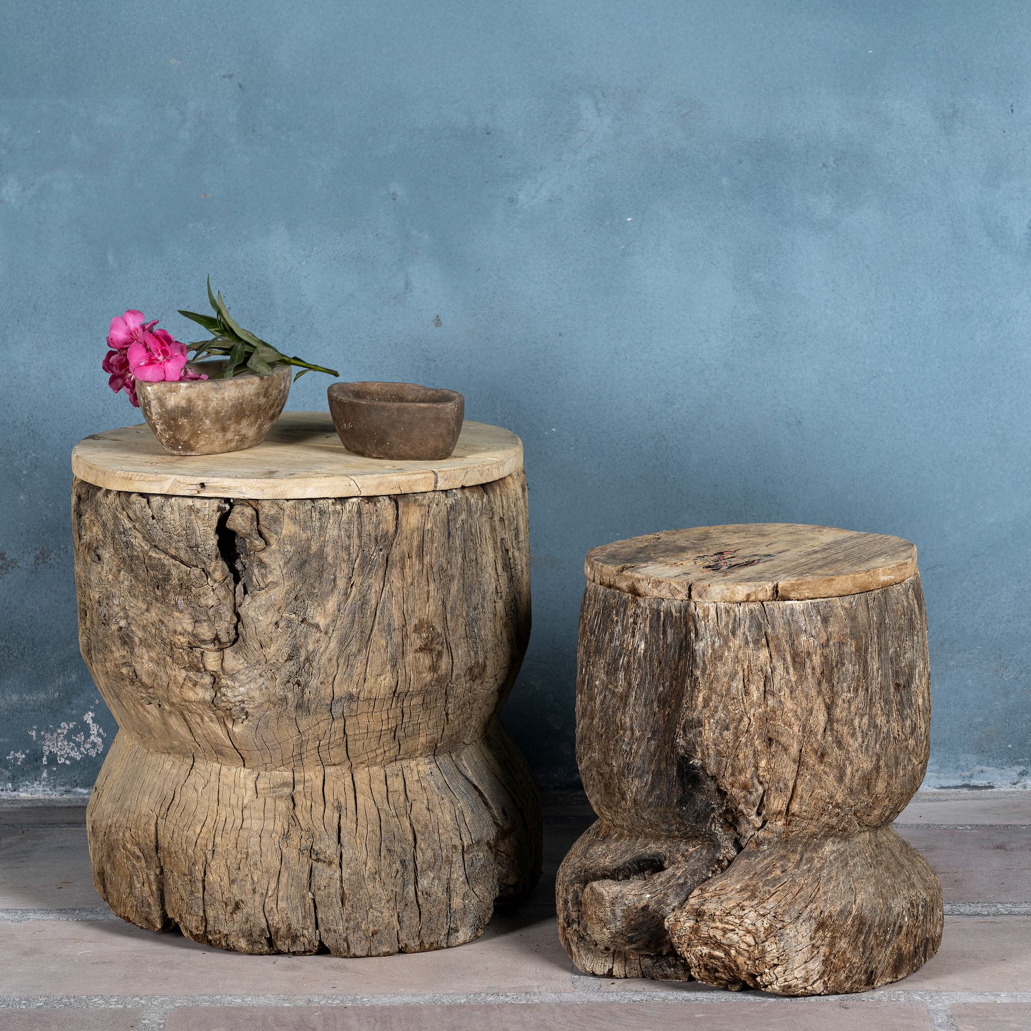 Side table in rustic minimalistic style made o reclaimed wood decorated with a stone bowl in front of a shabby blue wall.