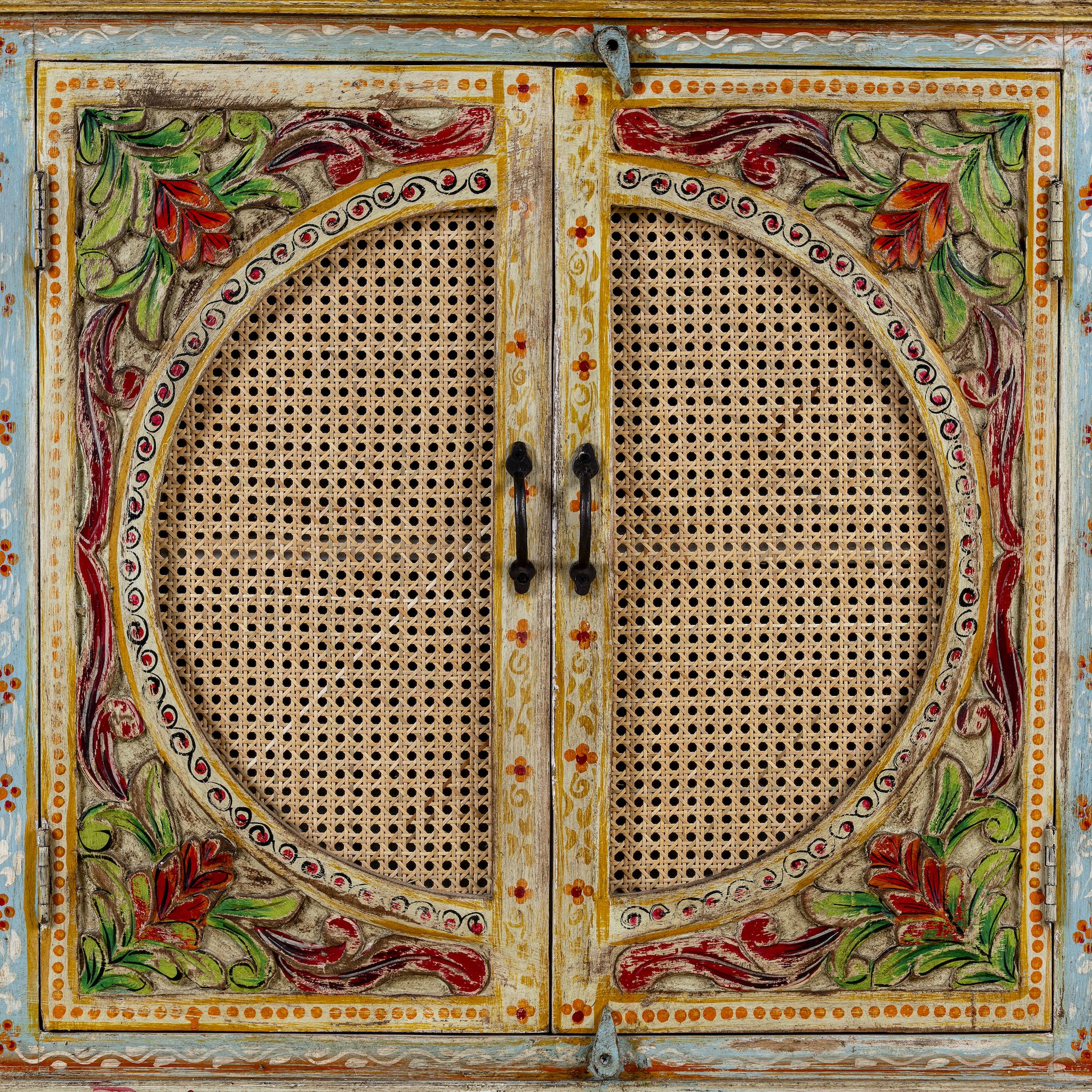 Detail view of a hand-painted, hand-carved cupboard made of mango wood with floral design and rattan inserts.