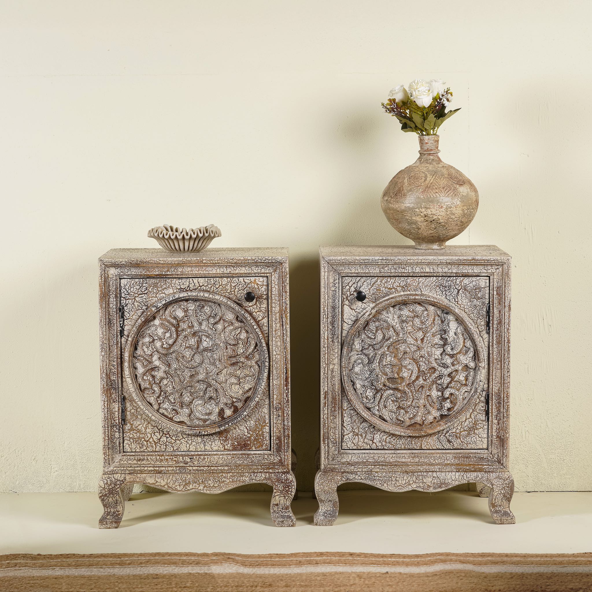 A pair of handcrafted bedside tables made from natural mango wood with intricate hand-carved floral motifs and a rustic antique finish.