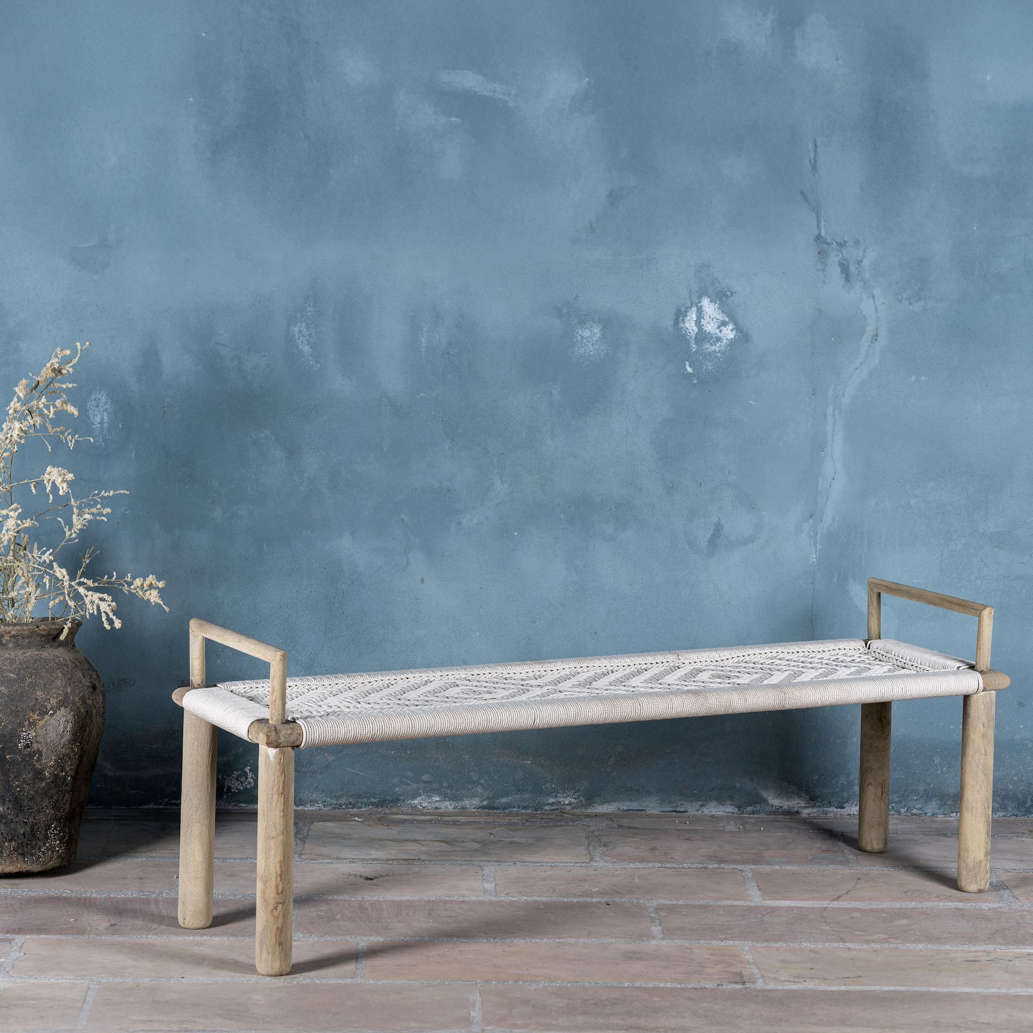 Side view of a Japandi style wooden bench with hand woven seating in a mediterrane scene.