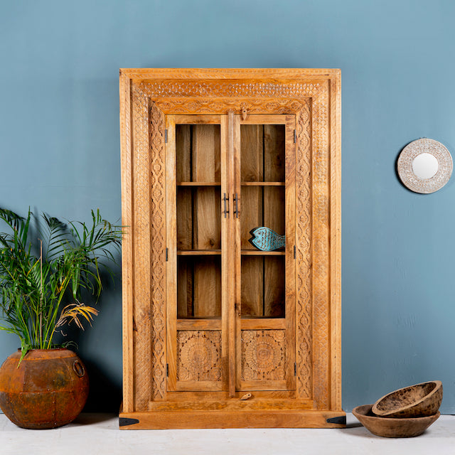 Hand carved display cabinet made from natural mango wood with floral detailing and glass-panelled doors; 180 × 110 × 40 cm.