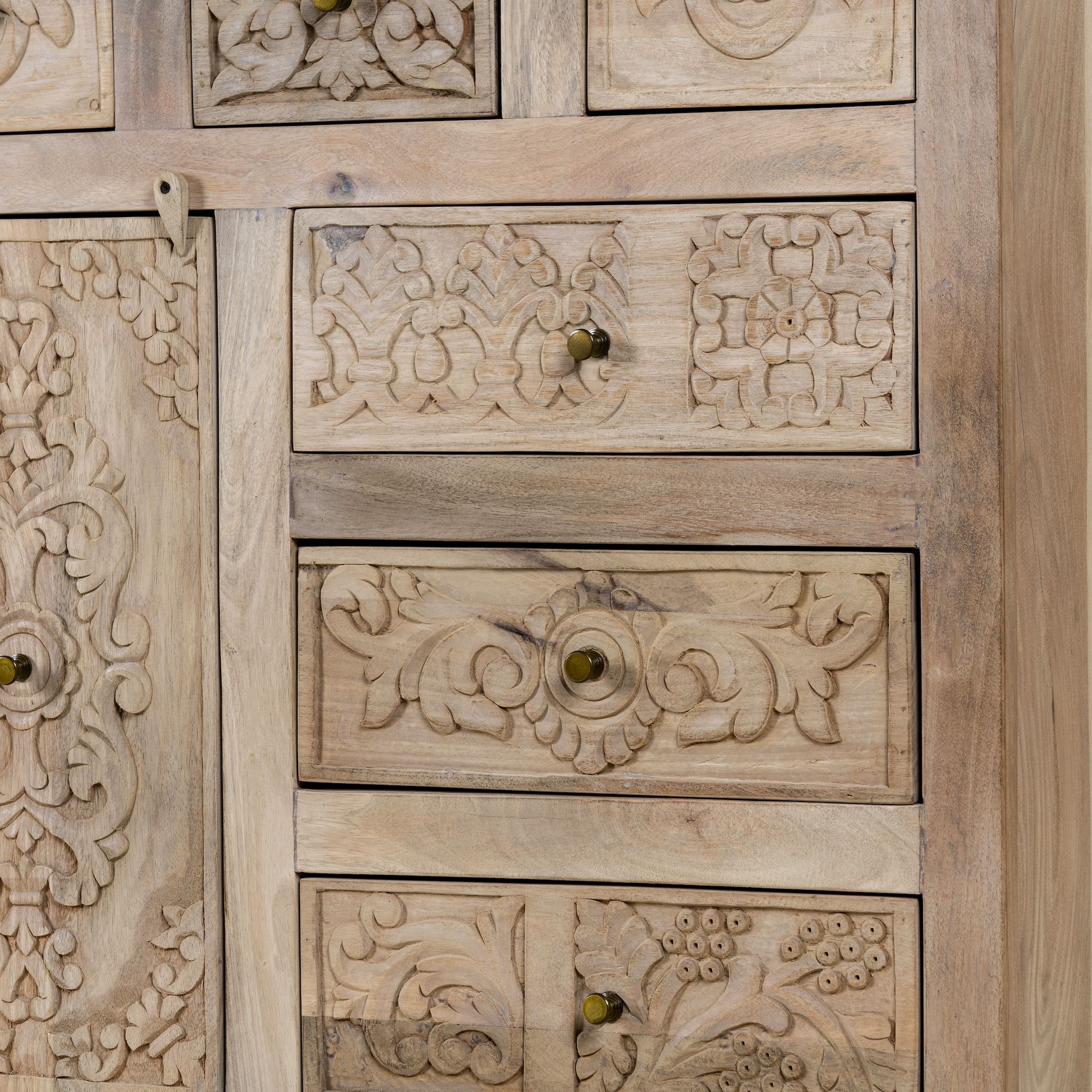 Close up view of a hand carved mango wood cupboard with 6 drawers and 1 door, iron fitted door knobs and floral carvings.