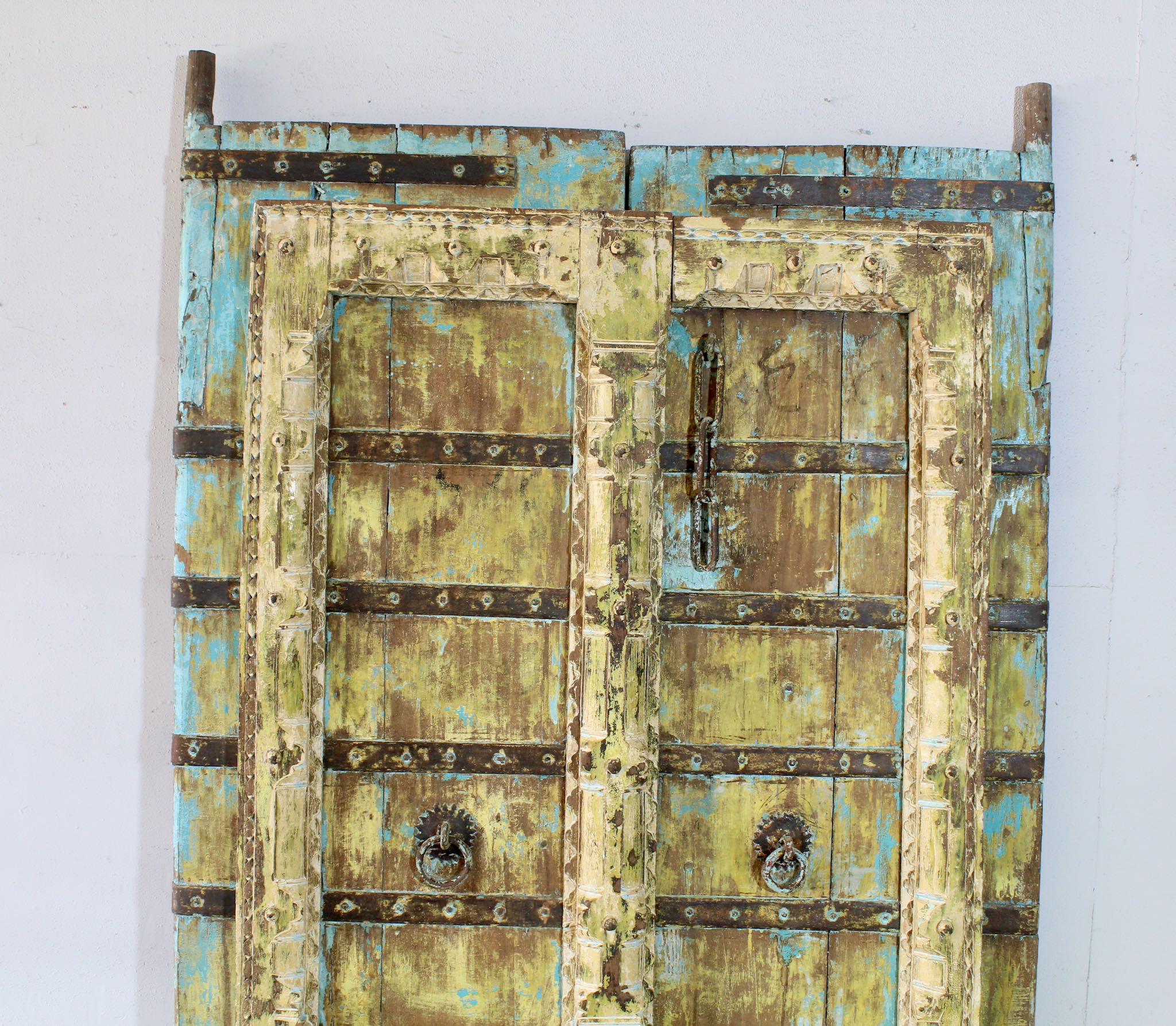 Close up image of an antique Indian teak and iron door with distressed turquoise and ochre patina, rustic vintage wall panels and bold vintage home decor.
