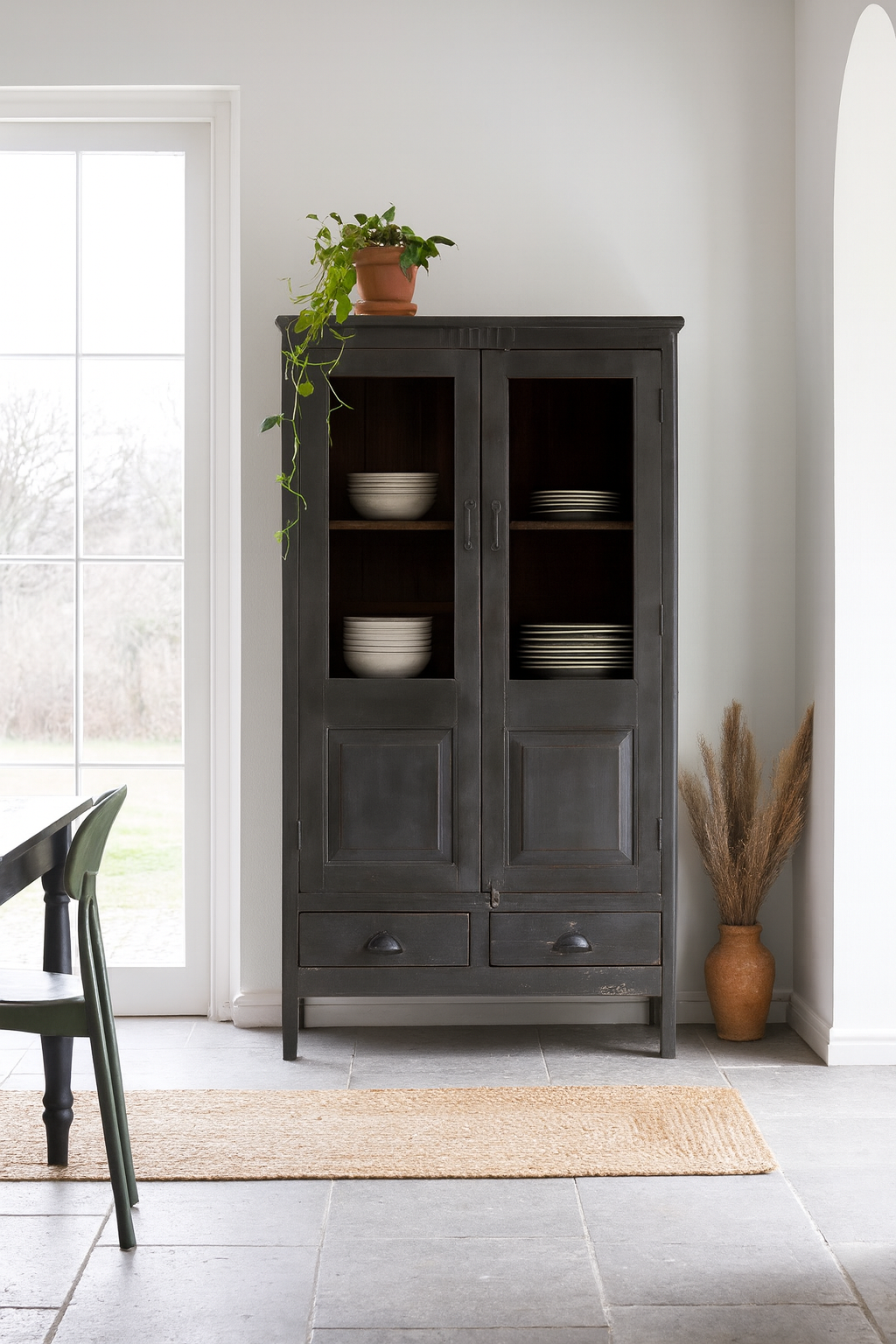 Lifestyle image of a refurbished teak wood cabinet with shabby chic grey finish and glass-panelled doors – sustainable furniture for elegant living and dining spaces.