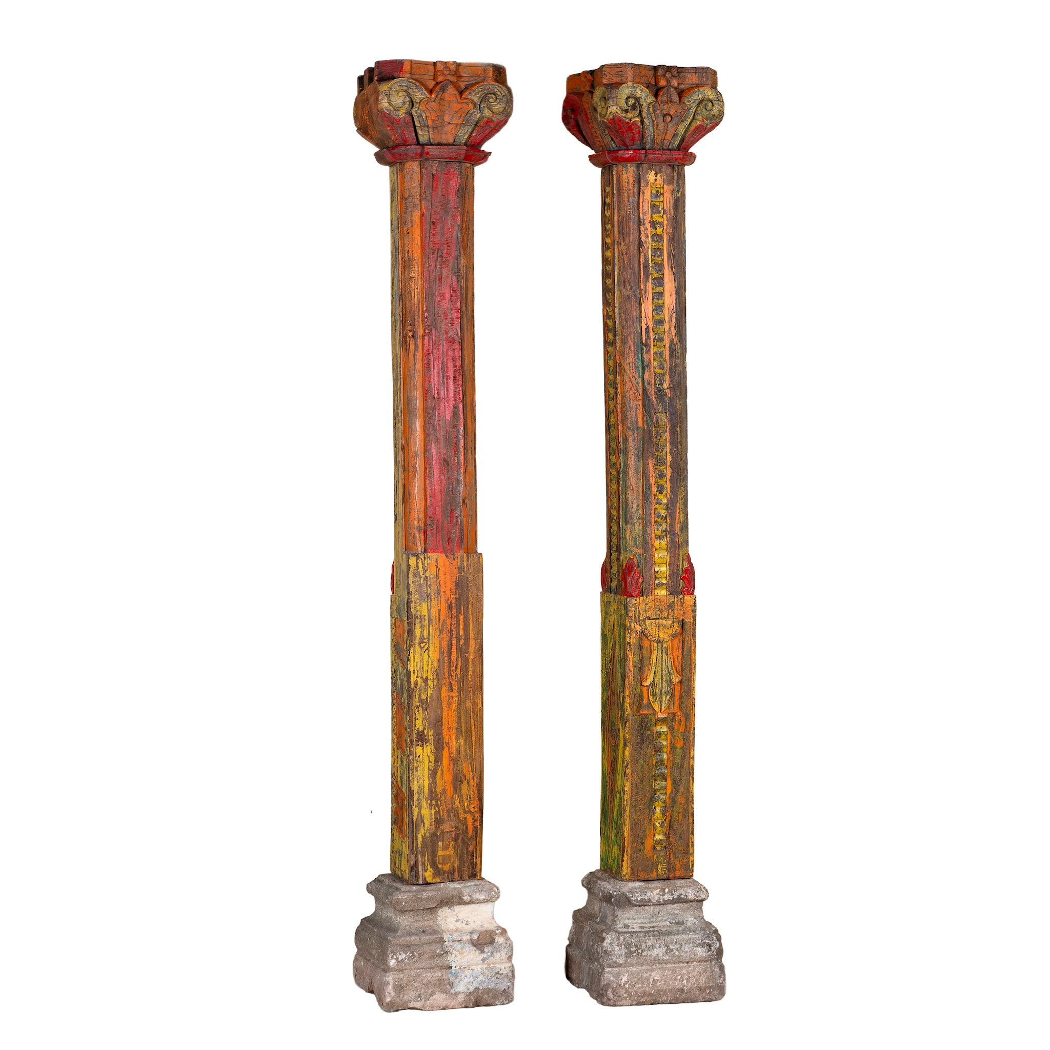 White background image of an antique pair of carved wooden house pillars with original stone bases, weathered multicolour finish, 210 cm high, vintage home decor and boho chic living room accents.