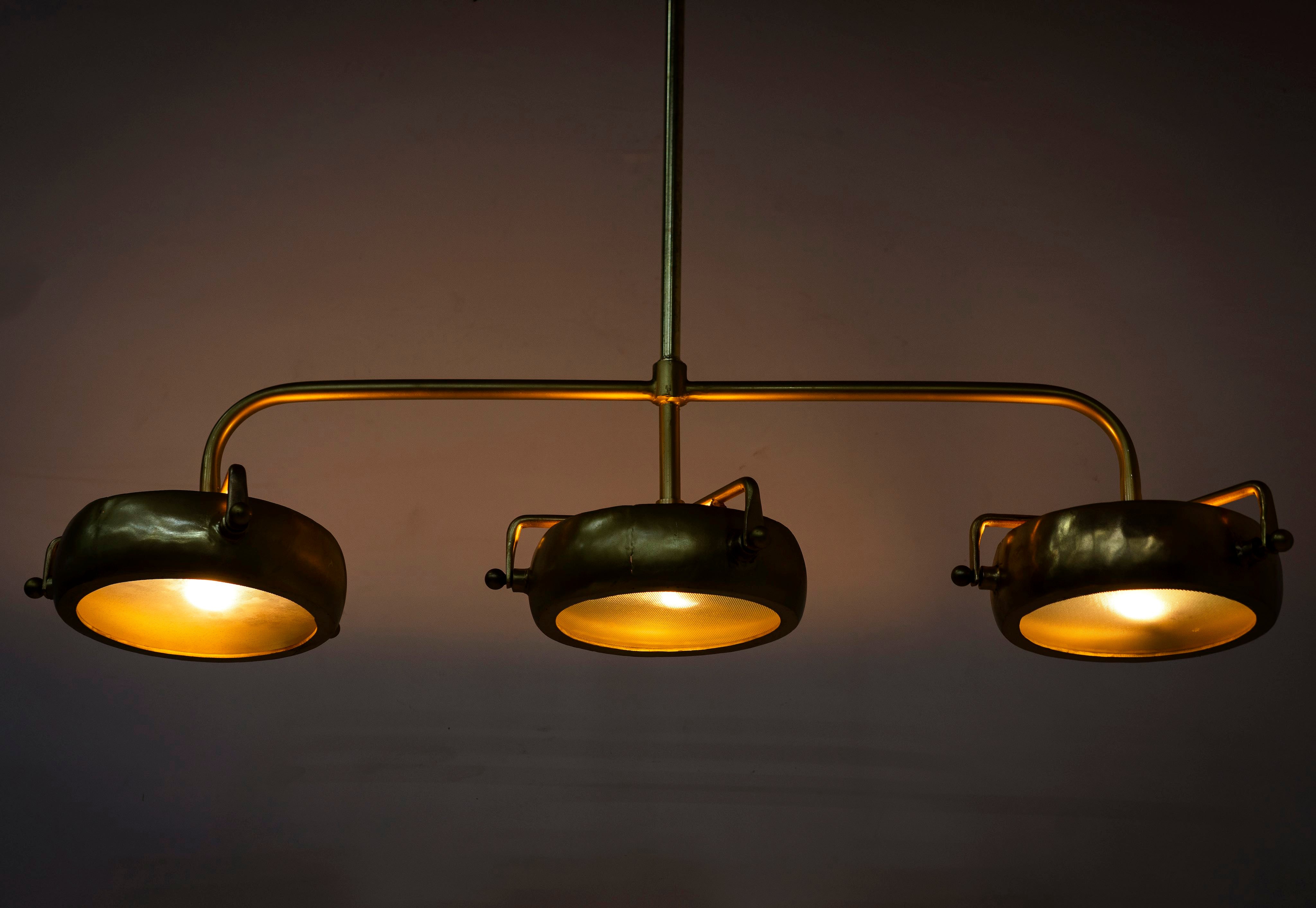 Image showing a lighted version of a elongated vintage pendant lamp with brass-plated frame and three clear glass shades – artsy lighting ideal for kitchens, dining rooms, or entryways.