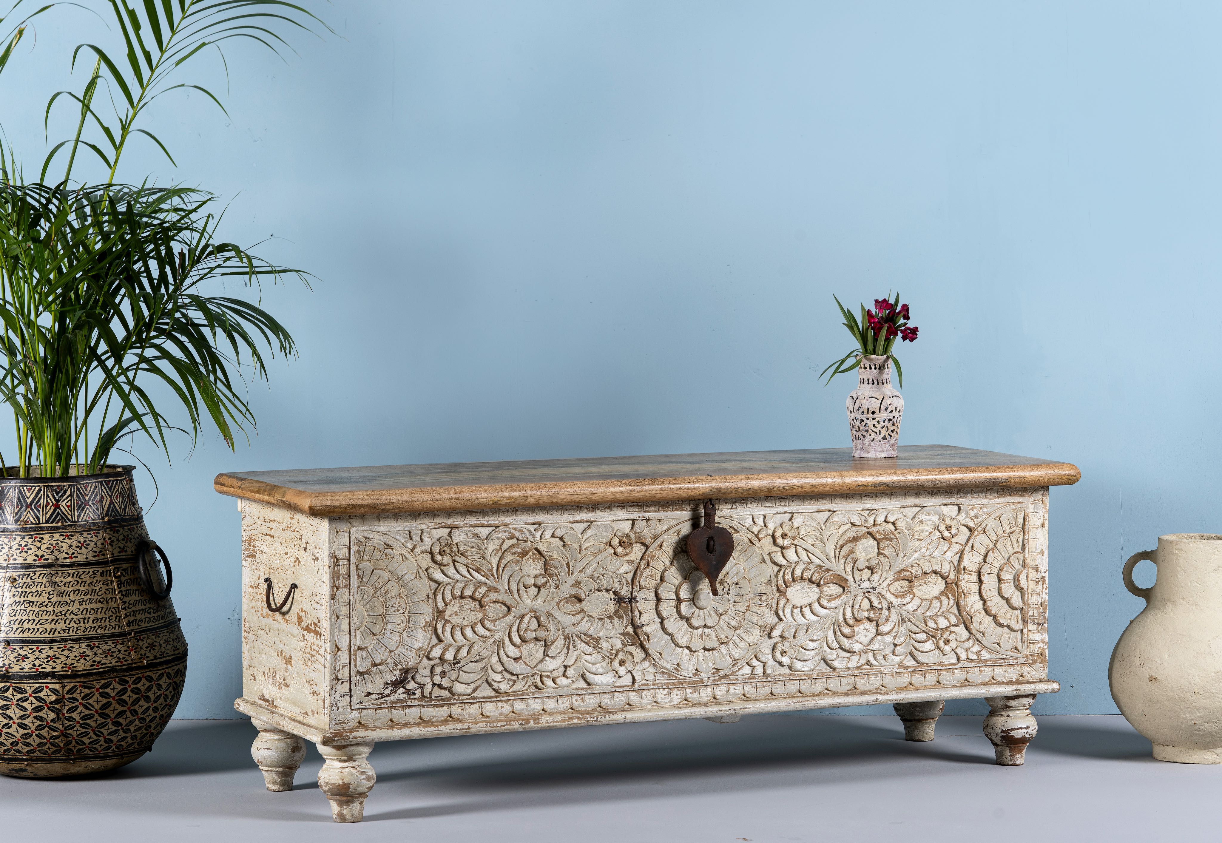 Side angle image of a hand-carved mango wood chest box with floral motifs, whitewashed finish, and iron handles – vintage home accessory for rustic and elegant interiors.