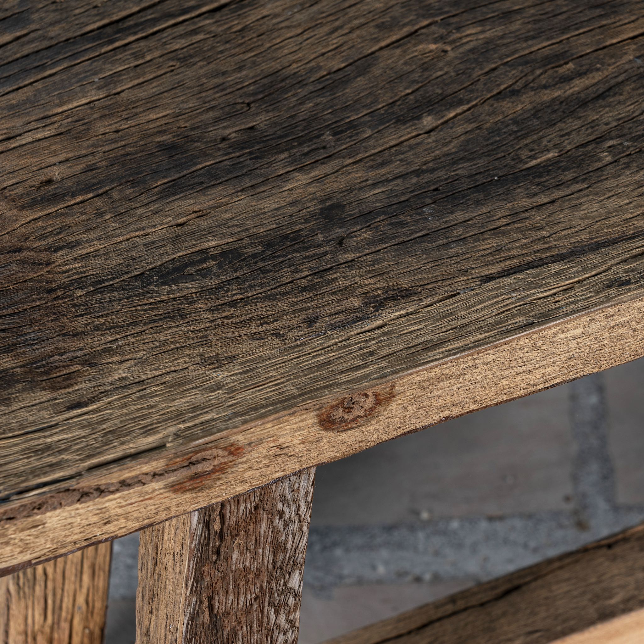Close up picture of a rustic driftwood bench made from reclaimed wood with aged finish and angled legs; handcrafted rustic wood furniture, 130 × 25 × 45 cm.