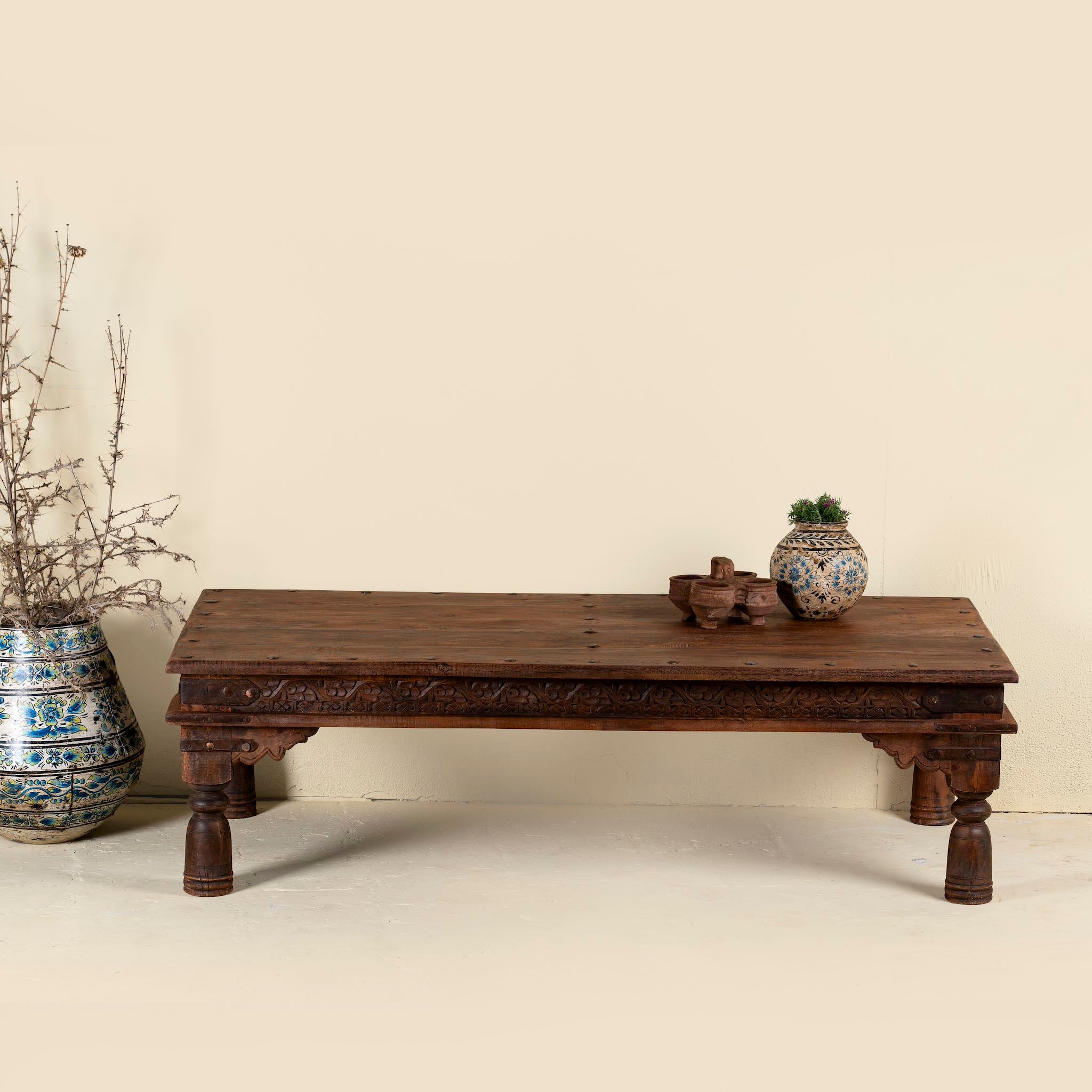 Lifestyle picture of a rectangular teak wood coffee table with hand-carved Indian detailing, reclaimed wood finish, and iron accents; 158 × 76 × 46 cm.
