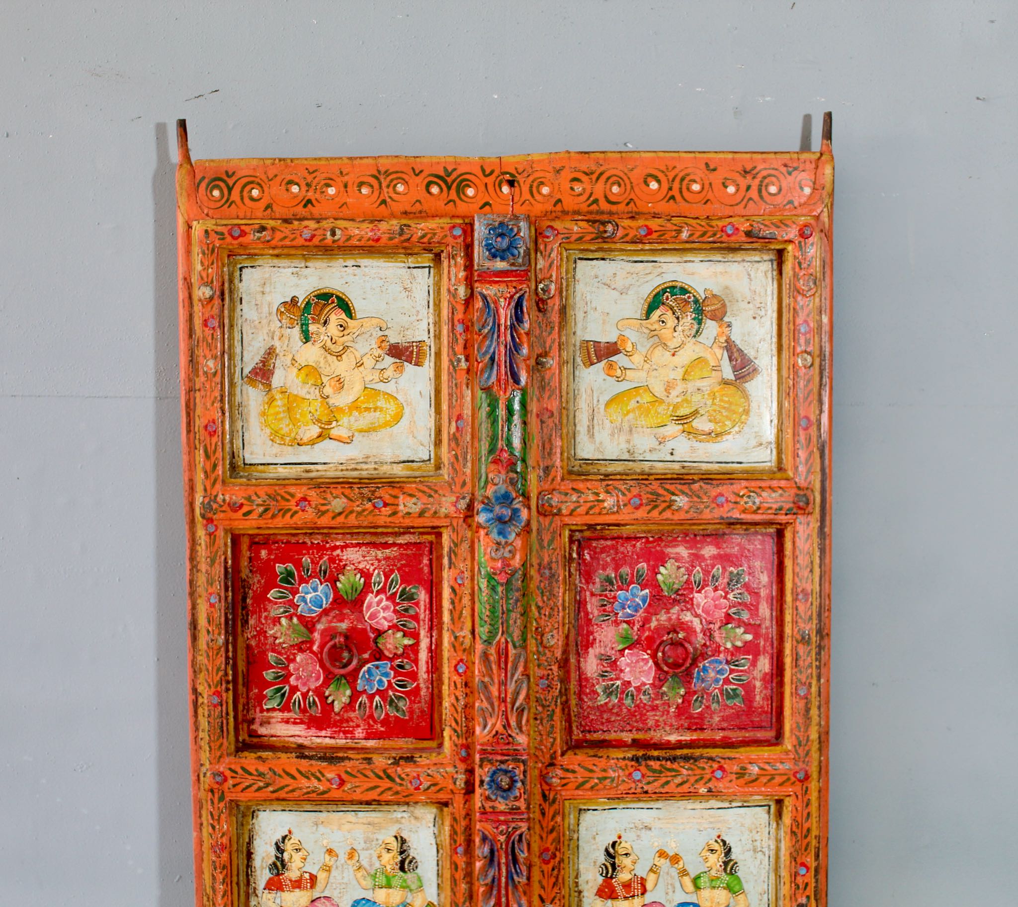 Close up image of a hand-painted Indian antique teak wood door with mythological and folk motifs, vibrant orange frame, vintage wall panels for spiritual and artistic home decor.