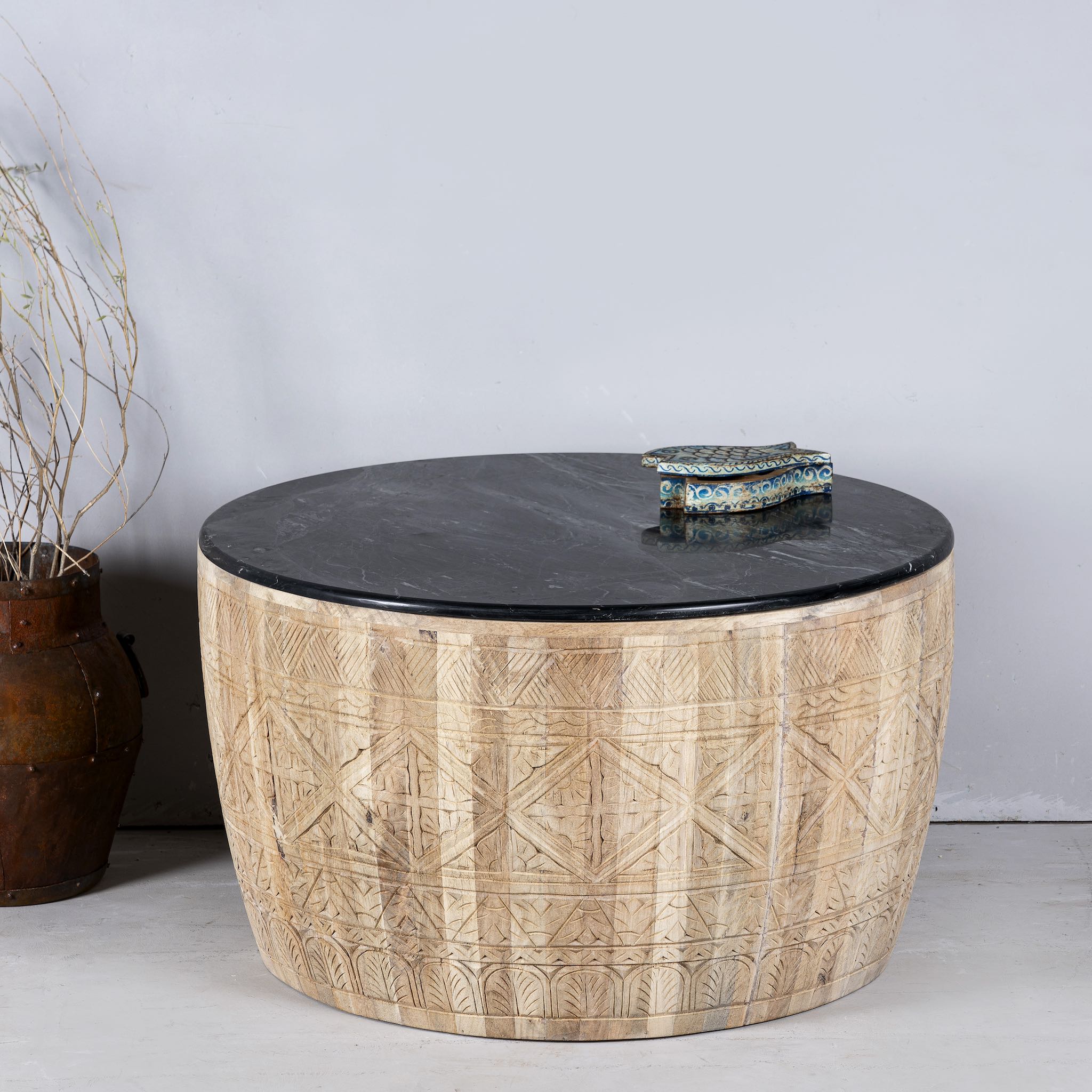 Front view of a elegant round hand carved coffee table made of sustainable Mango wood with floral design and black marble top.