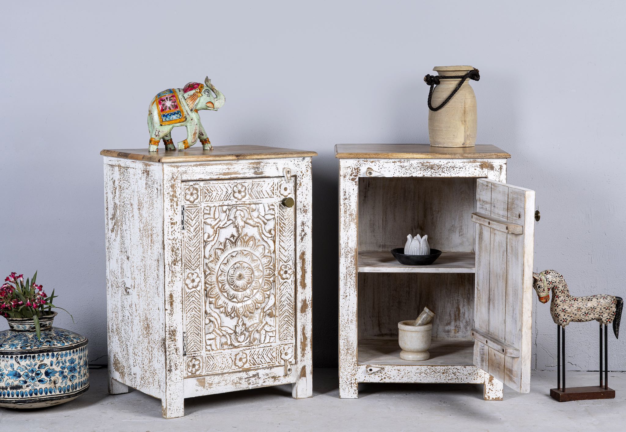 Side angle image with open door of a set of two hand carved bedside tables with mandala and floral motifs; reclaimed wood in white washed furniture style, 50 × 40 × 72 cm.