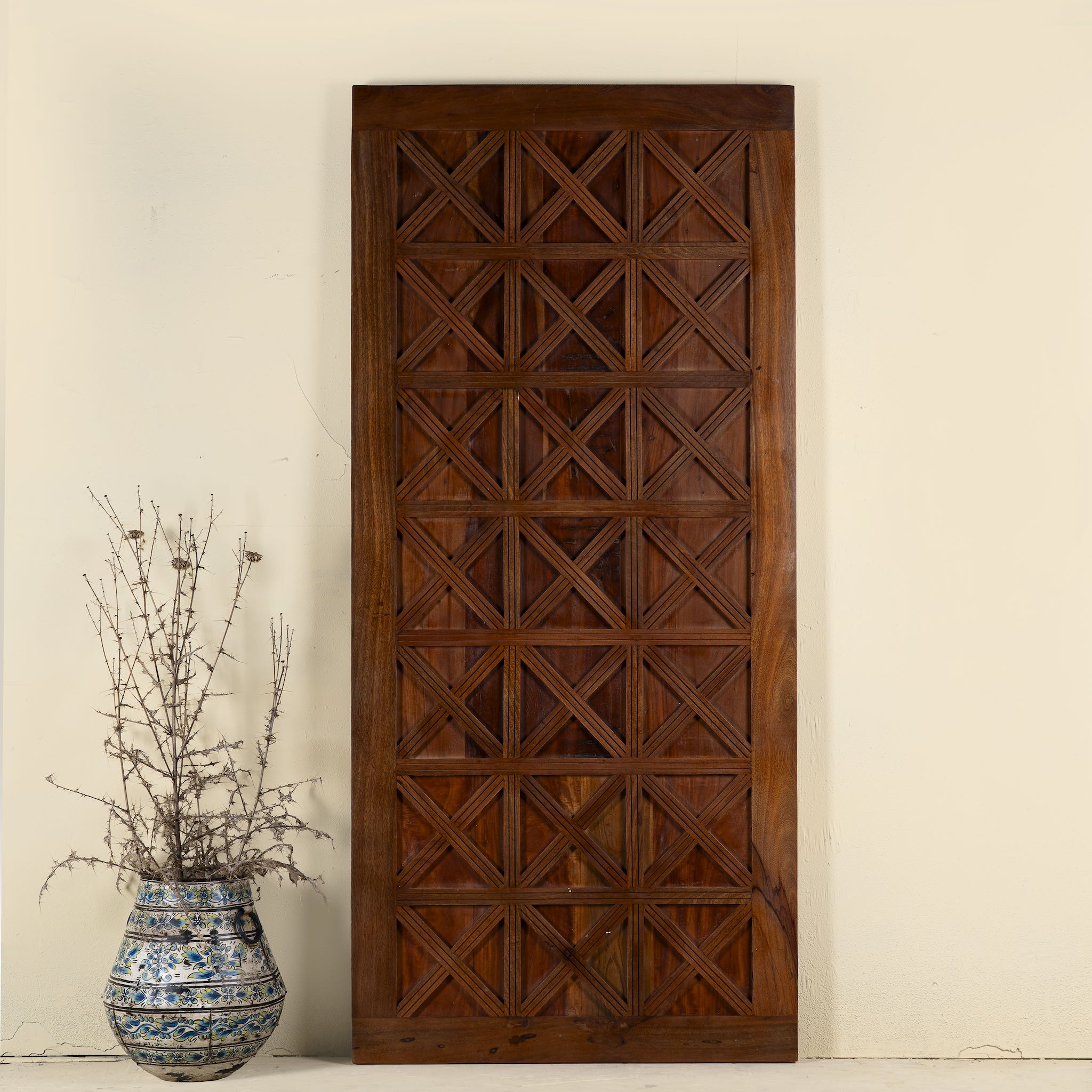 Wooden panel with geometric pattern next to a decorative vase on a light background
