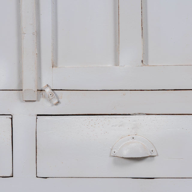 Close up image of a shabby chic teak wood cabinet with glass doors, drawers, and compartments – sustainable living room furniture crafted from refurbished teak wood with a soft white finish.