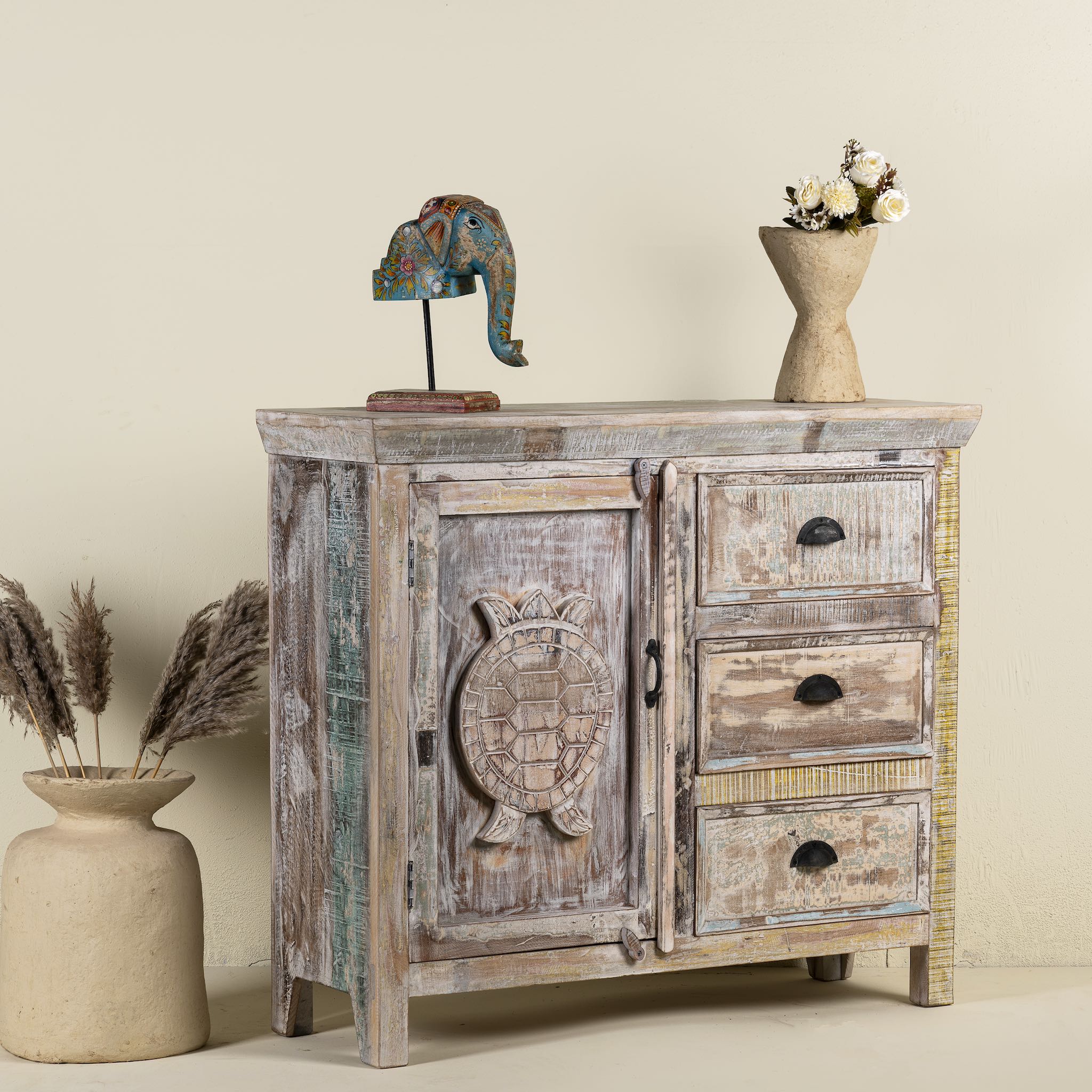 Side angle image of a handcrafted cupboard made from reclaimed wood with a carved turtle motif and pastel finish; vintage furniture and sustainable furniture, 110 × 96 × 40 cm.