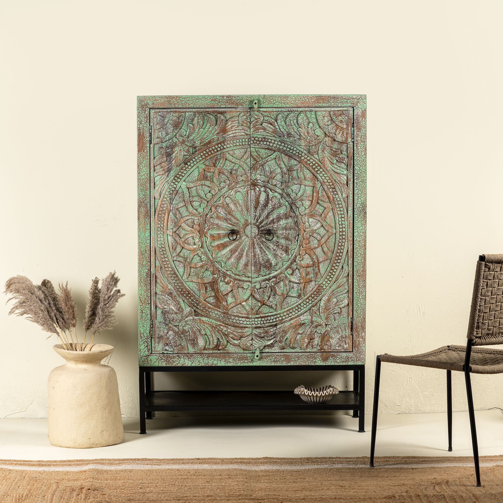 Carved mango wood cabinet with floral hand-carving, distressed green finish, iron stand, 100 × 40 × 150 cm.