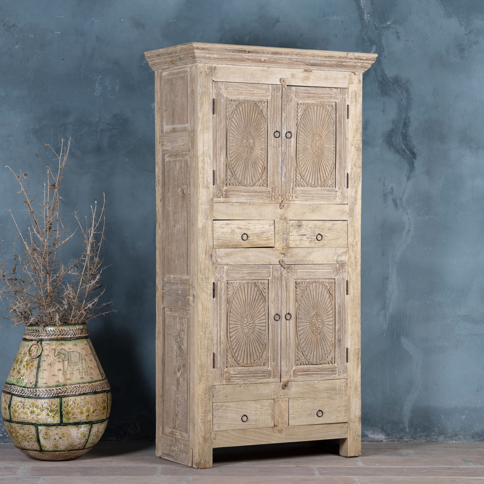 Side angle view of a wardrobe made from reclaimed wood with a sandblasted finish, featuring four carved doors, six drawers, and a light, rustic look in timeless Ibiza style.