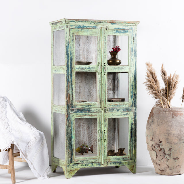 Side angle image of a refurbished teak wood showcase with distressed green finish – sustainable furniture with boho style interior appeal and glass-panelled storage.
