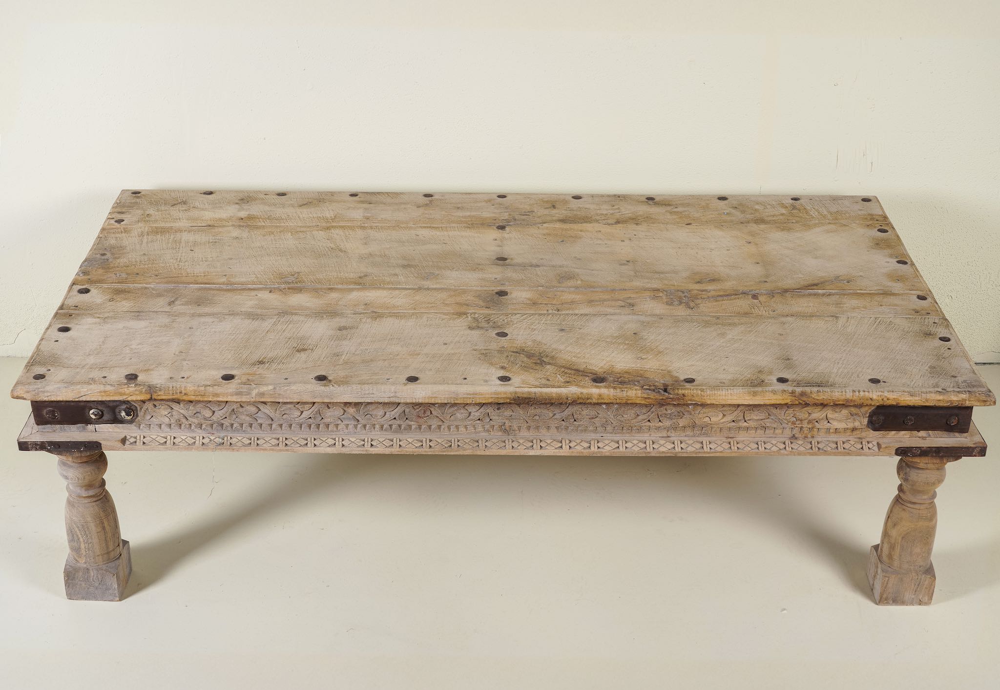 Close up of the table top of a rustic coffee table Ritvik made from old reclaimed teak wood, featuring a weathered finish, turned legs, decorative carved apron, and visible metal rivets, styled with earthy decor in a minimal interior setting.