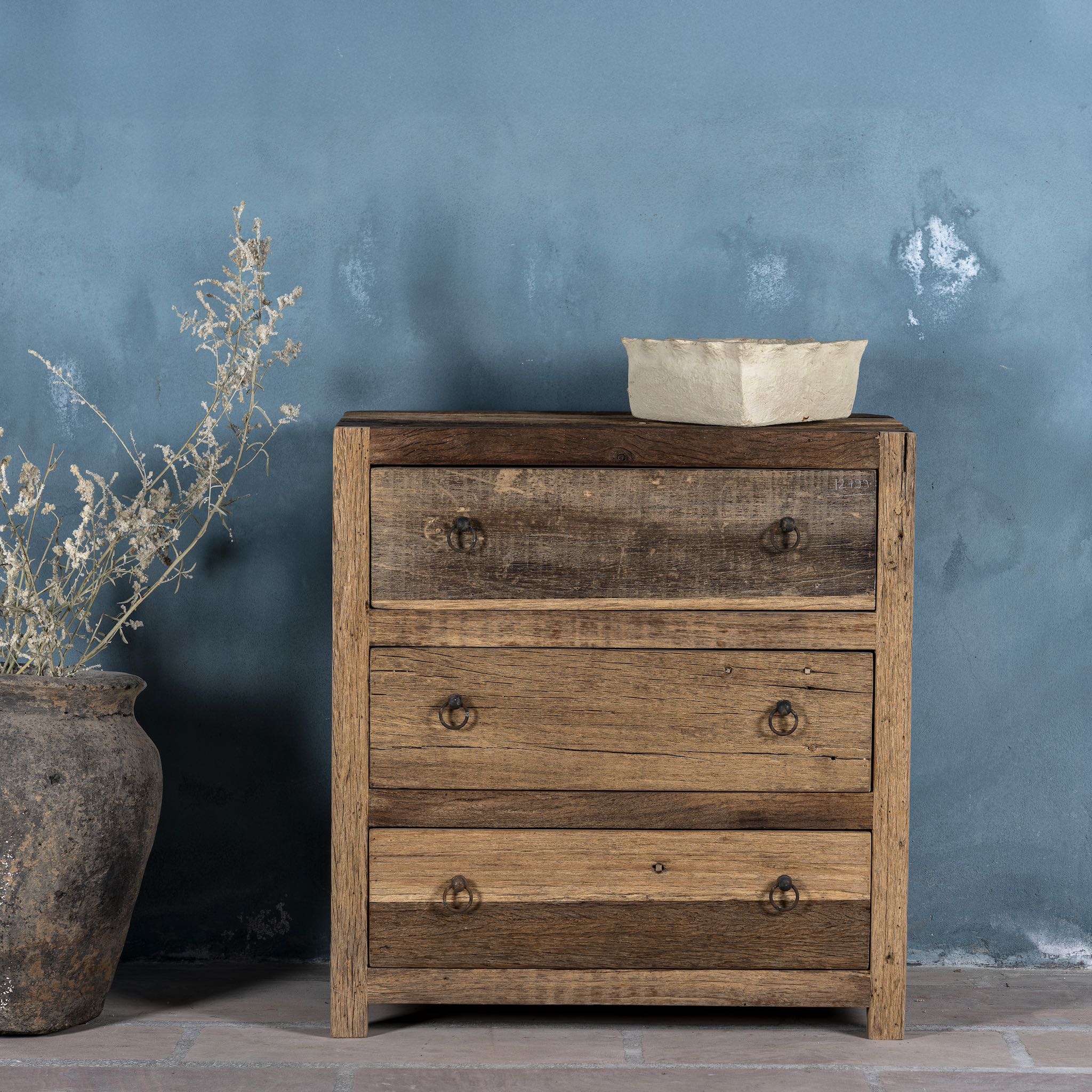 Front view image of a three-drawer dresser in Driftwood/Wabi Sabi style made from recycled old wood, featuring a naturally weathered finish with visible grain patterns and metal ring pull handles for a rustic, handcrafted look.