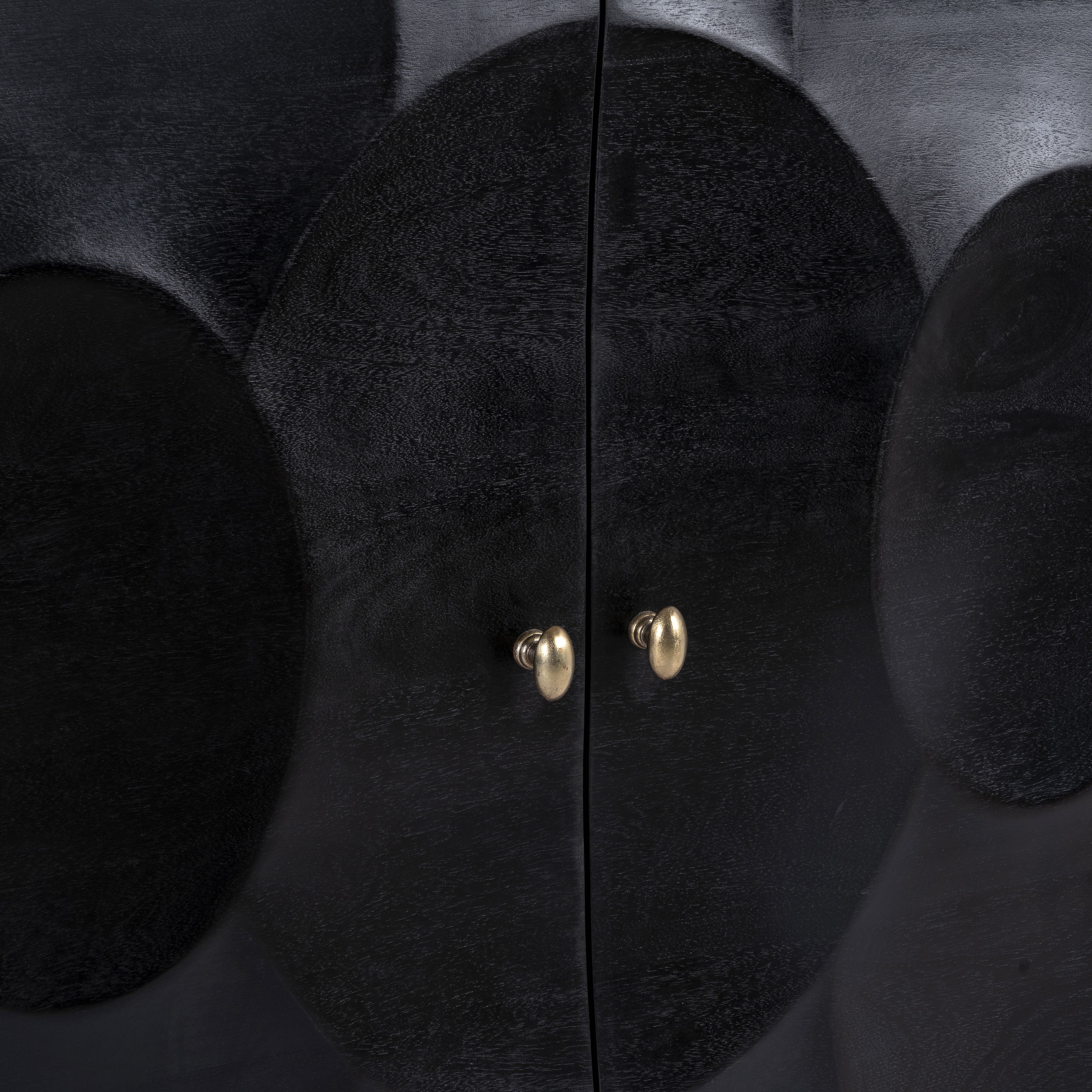 Close up image of a black mango wood cabinet with carved circular patterns and brass-plated iron base, 91 × 43 × 111 cm.