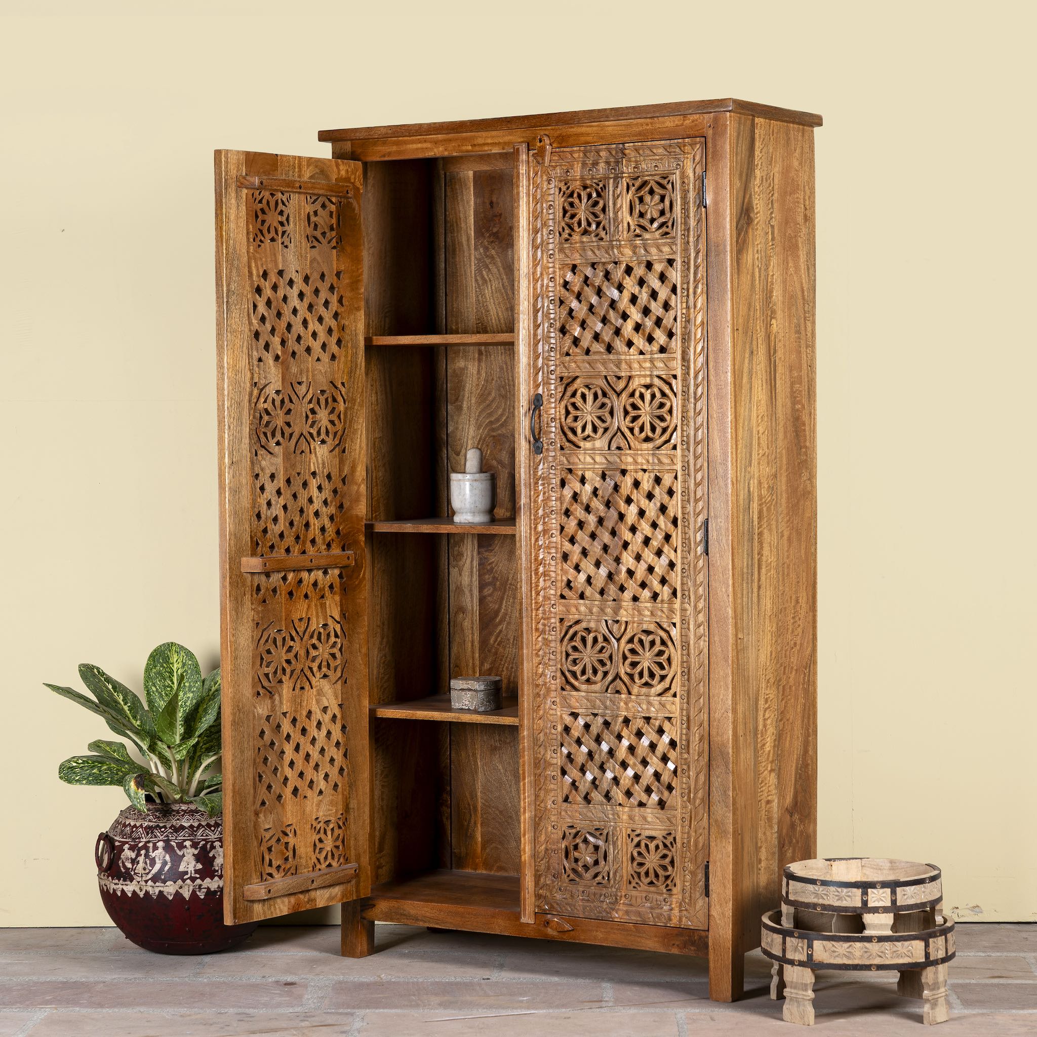 Side angle image showing a open door of a hand-carved mango wood wardrobe with floral and lattice motifs – a detailed piece of carved wood furniture ideal for natural mango wood interiors.