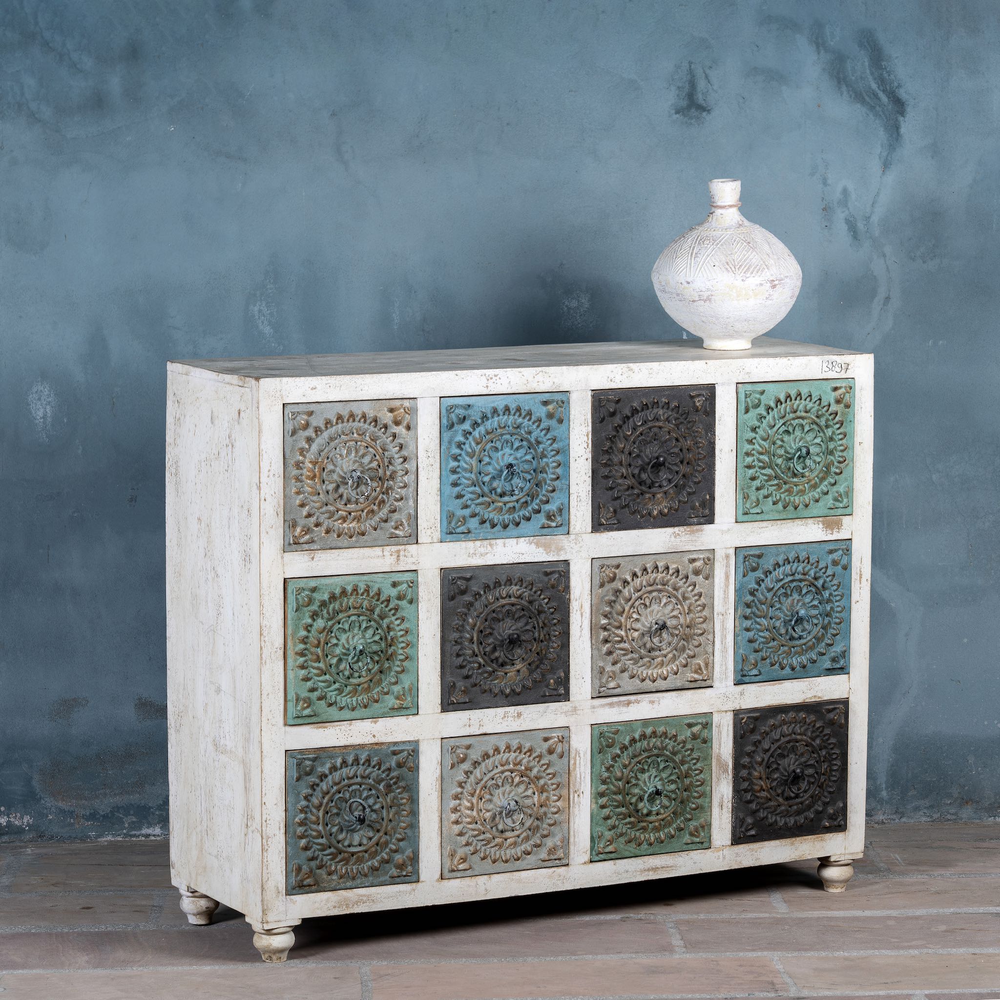 Side angle image of a carved mango wood chest of drawers with twelve multicolour floral drawer fronts, 124 × 40 × 102 cm.